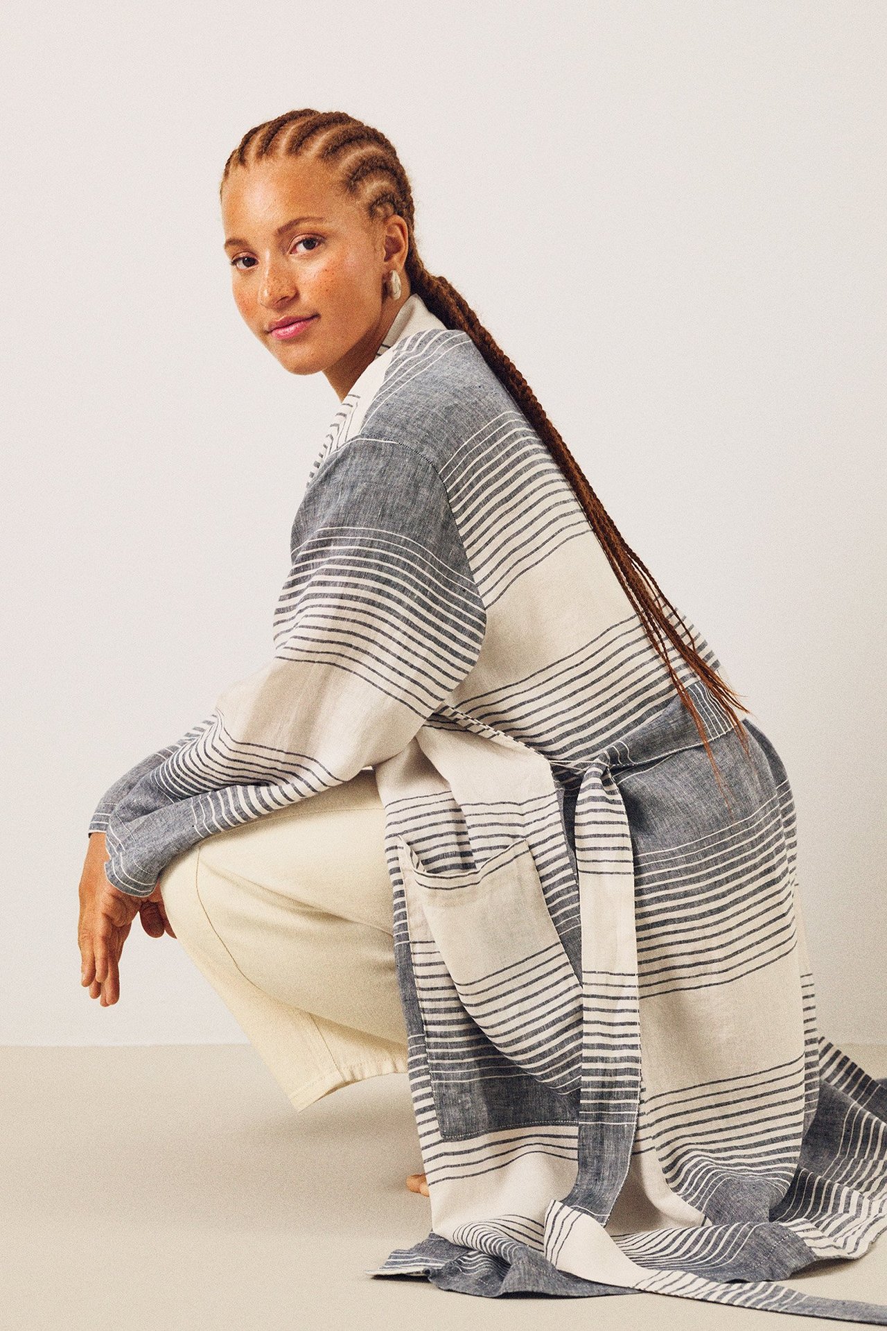 Front-side av kvinne i mørkeblå og hvitstripet linkimono med knytebelte og lysebeige bukser.
