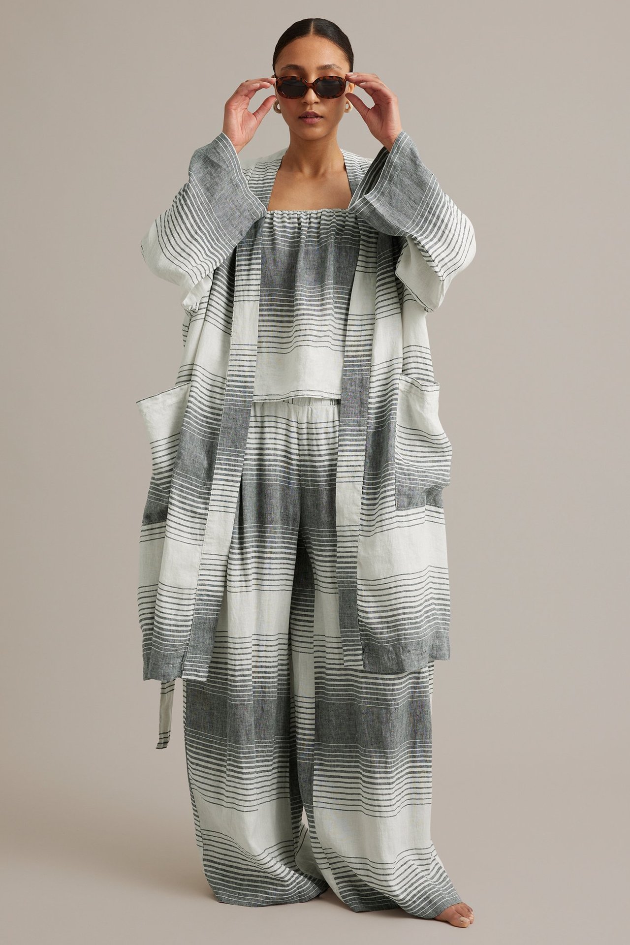 Forfra: Kvinne i mørkeblåstripet linkimono med lommer og knytebelte, over matchende topp og bukser, justerer solbriller.