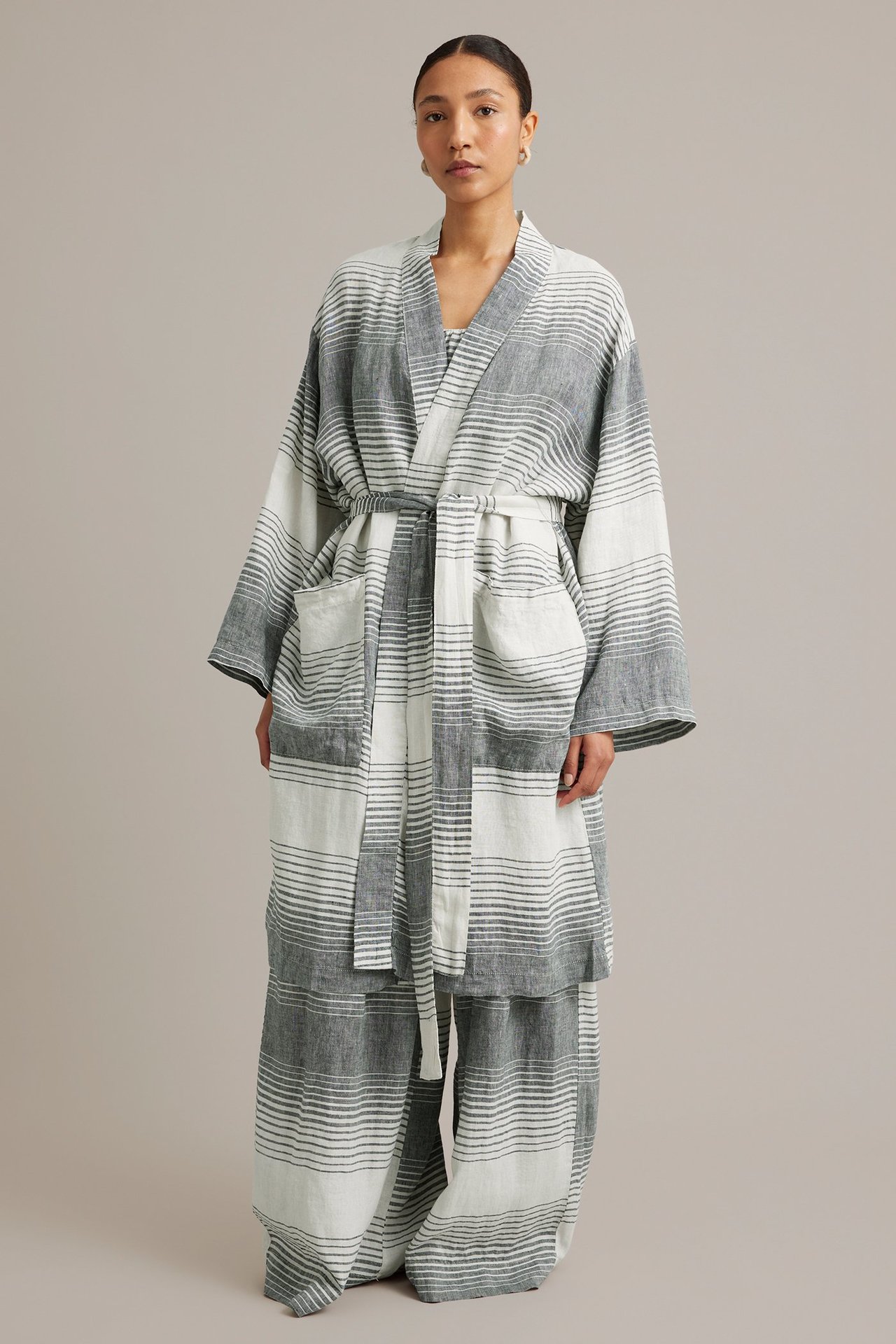 Kvinna bär en mörkblå och vitrandig linnekimono med knytskärp och fickor, över matchande byxor.