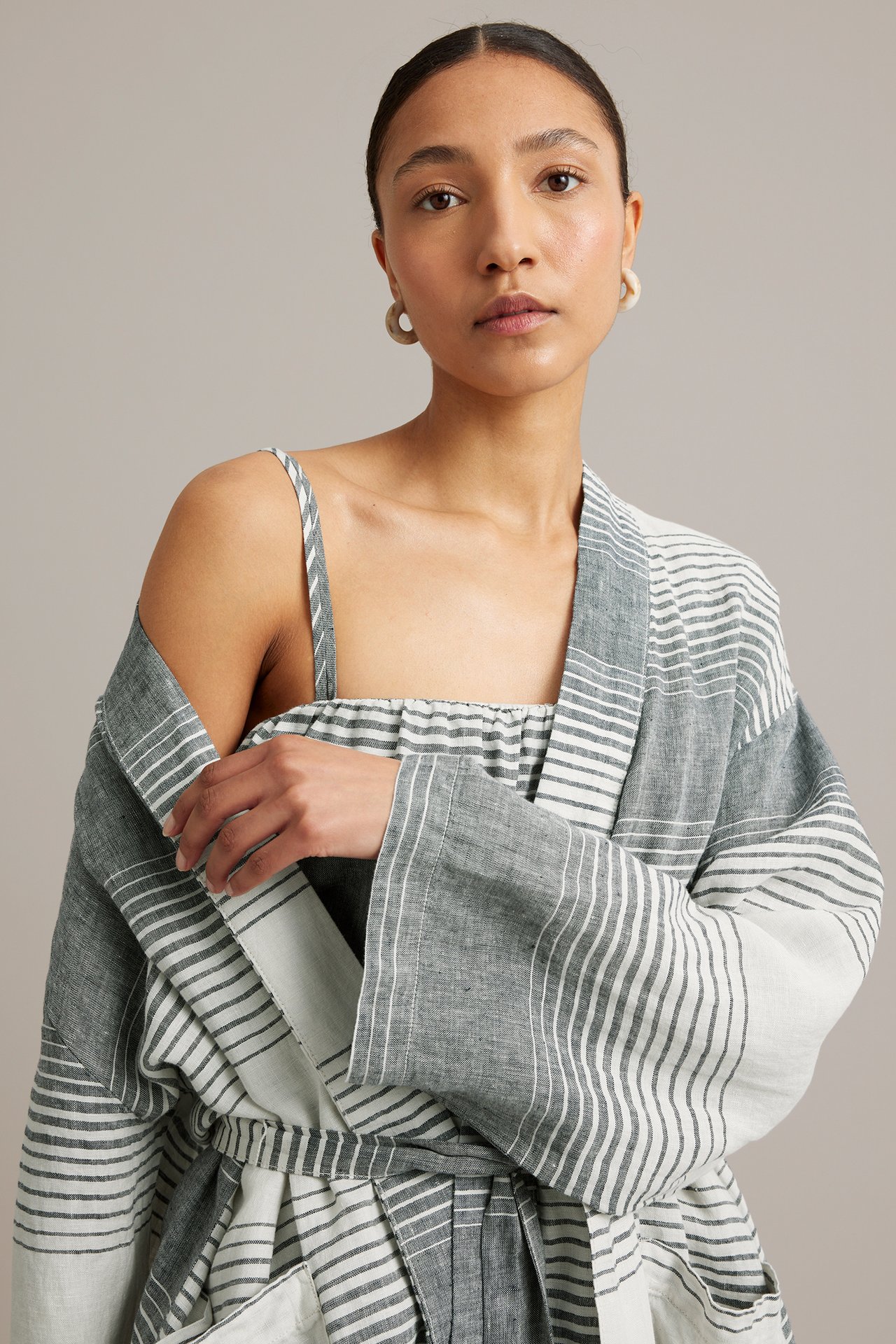 Kvinna i mörkblå, vitrandig linnekimono med knytskärp över matchande topp, örhängen. Framifrån.