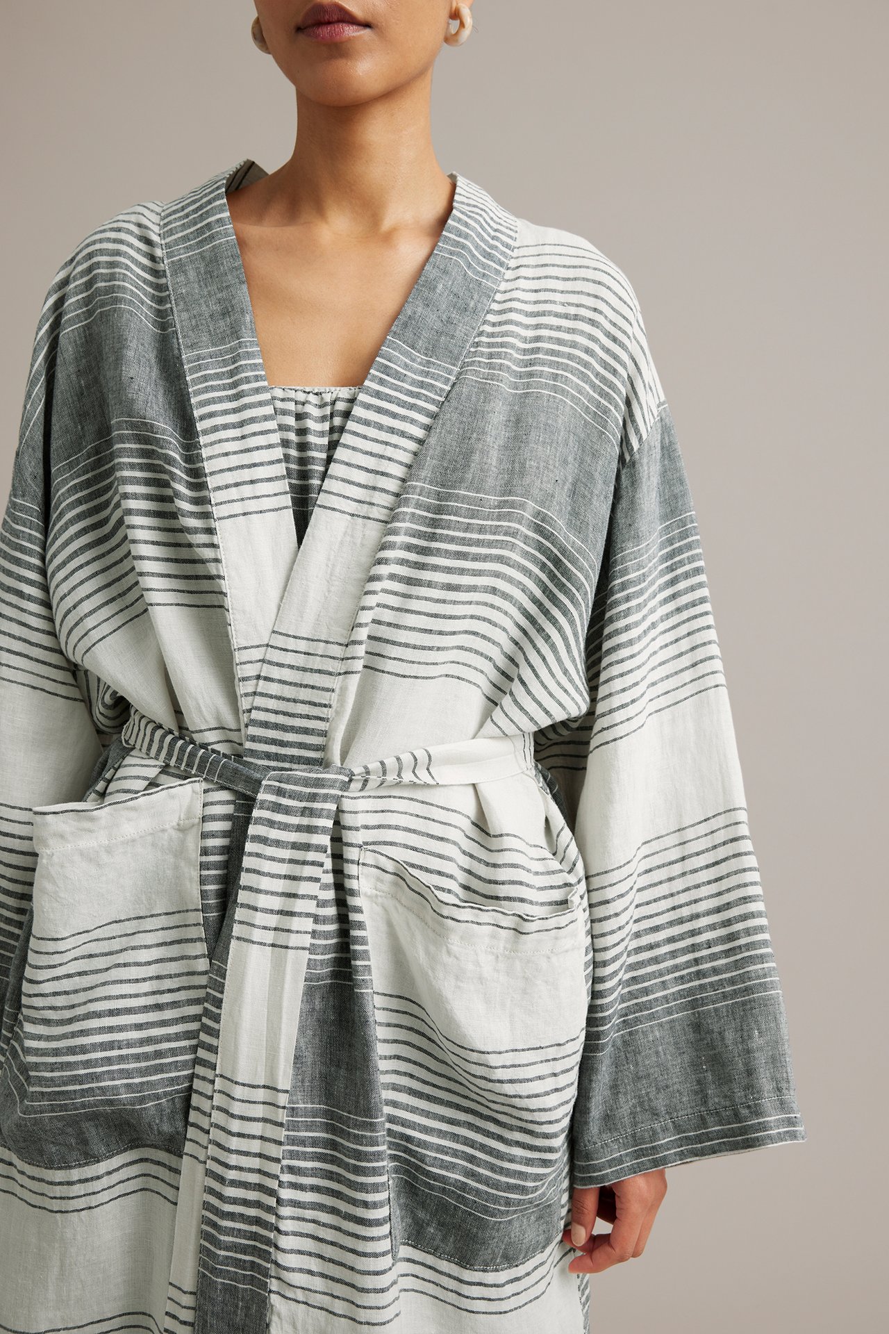 Framifrån: Kvinna i mörkblå och vitrandig linnekimono med knytskärp och fickor.