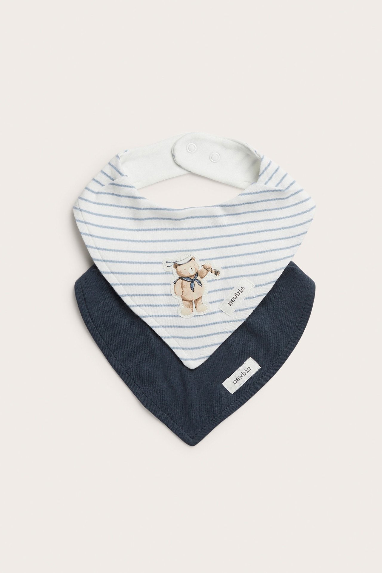 Widok z przodu: Dwa bawełniane śliniaki bandany. Jeden biały w paski z misiem marynarzem, jeden granatowy, zapinane na zatrzaski.