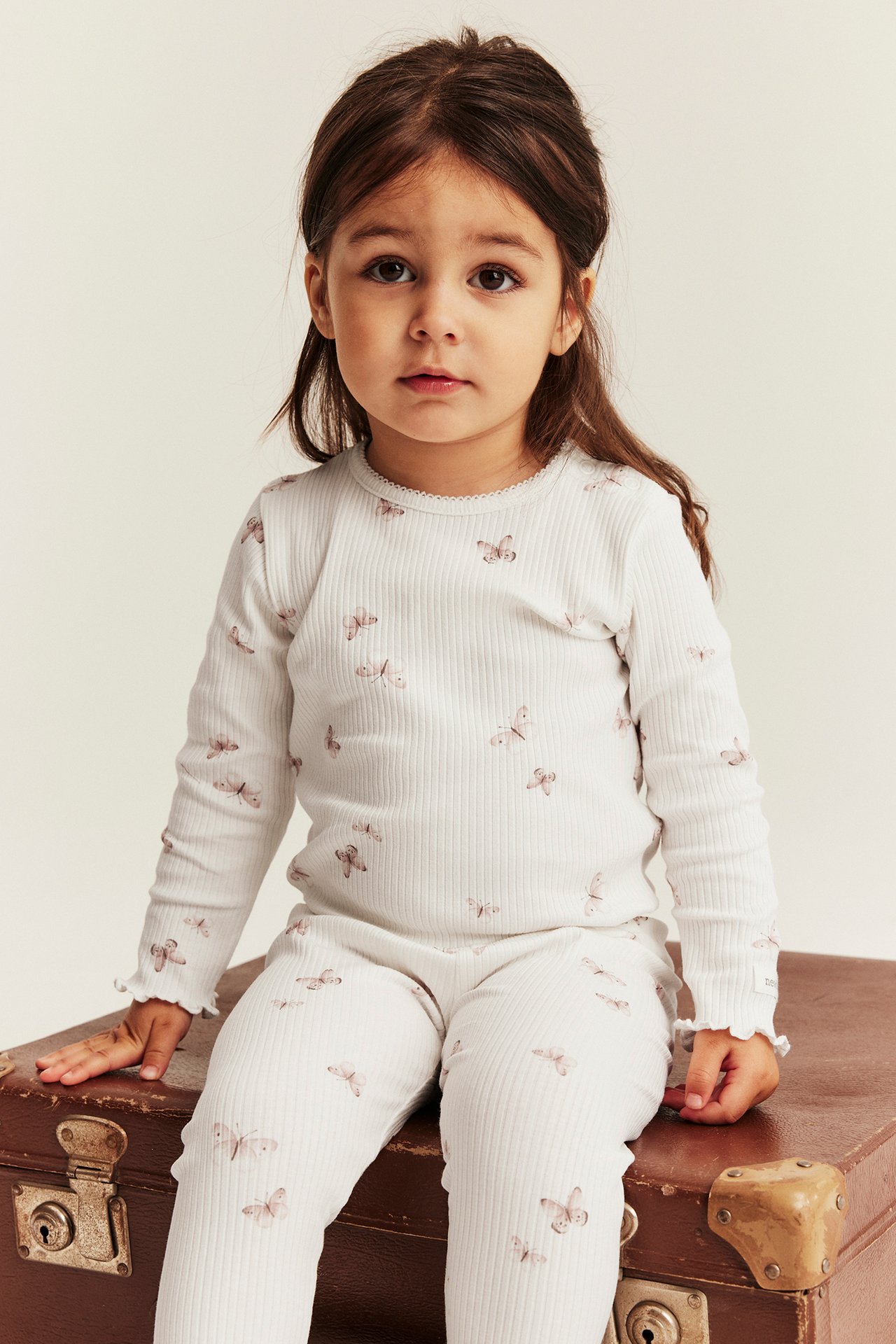 Frontbilde av et barn i en offwhite ribbet langermet body med sommerfuglmønster og matchende leggings.