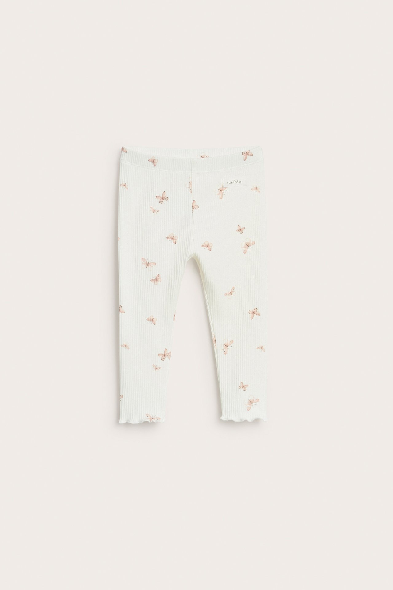 Forfra: Ribbede baby-leggings i offwhite med lysebrunt sommerfuglmønster og bølgete kanter.