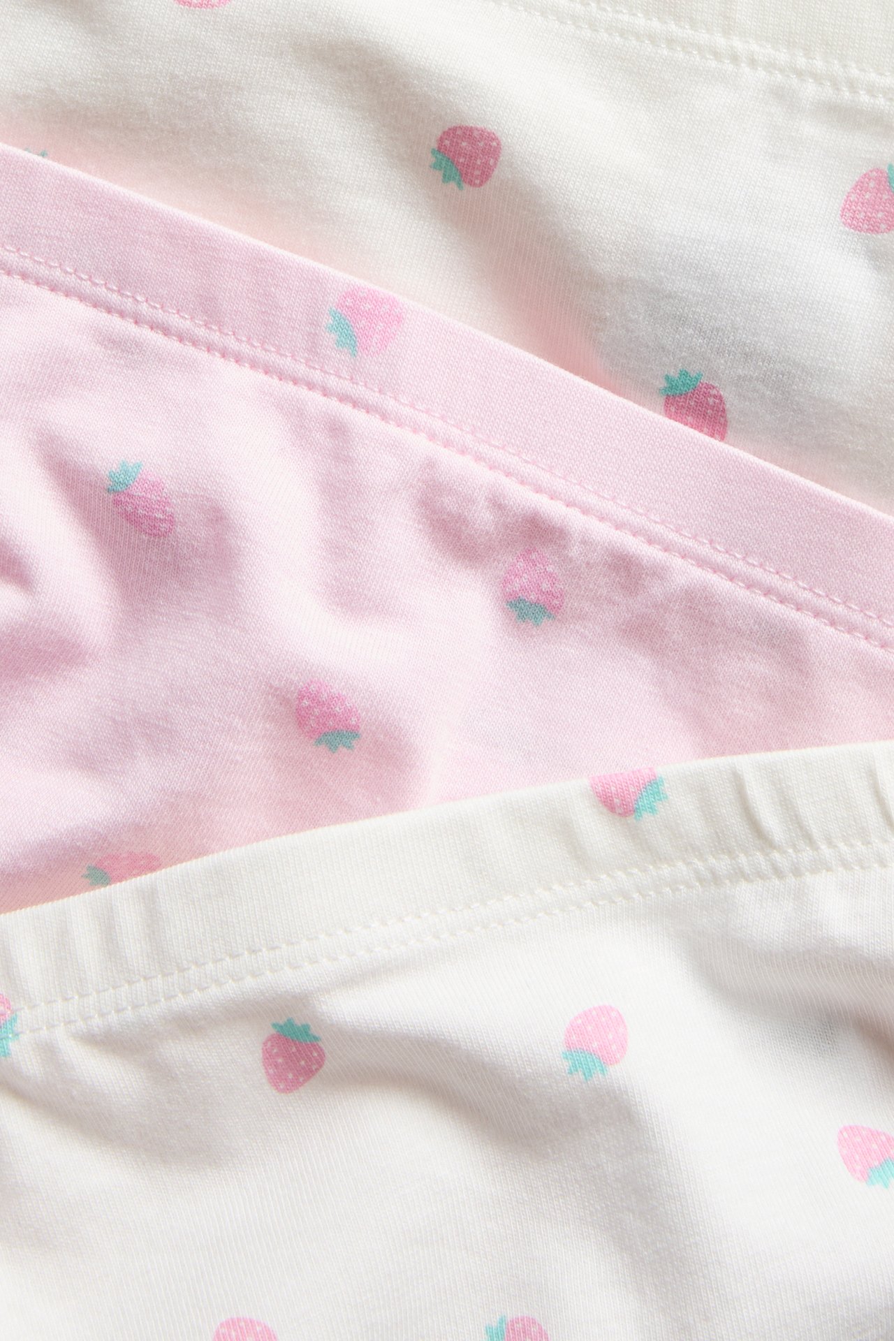 Lähikuva kolmesta lapsen bokserista: yksi pinkki, kaksi valkoista, mansikkakuviolla.