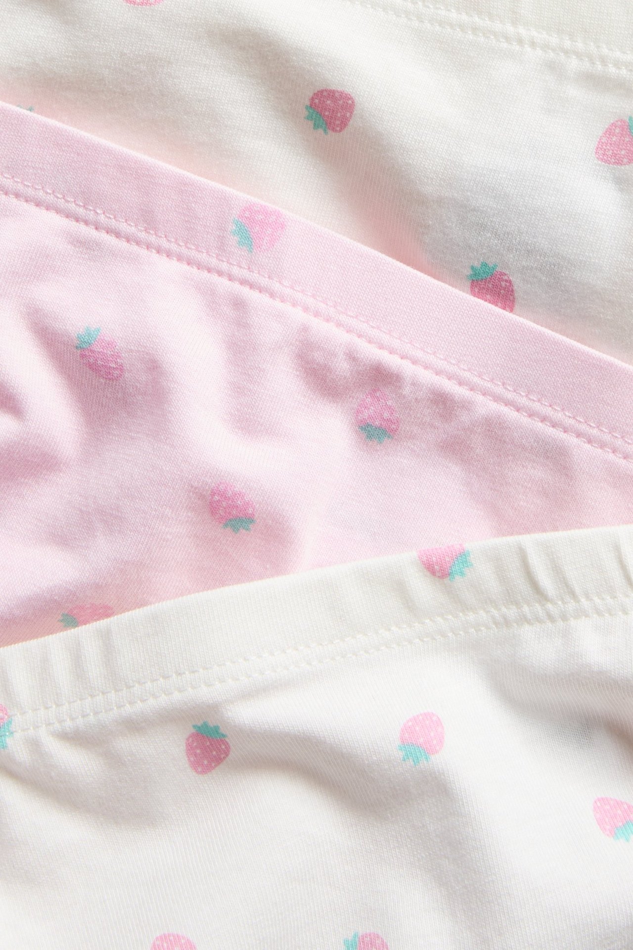Lähikuva kolmesta lapsen bokserista: yksi pinkki, kaksi valkoista, mansikkakuviolla.