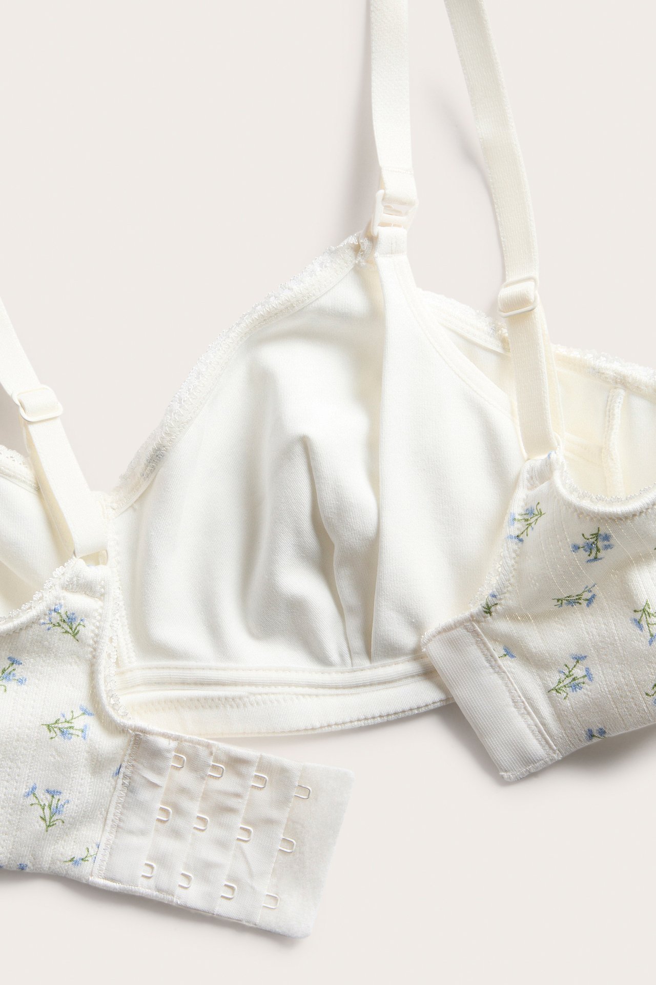 Nærbilde av en offwhite pointelle-ribbet amme-BH med blått blomstermønster og hektefeste.