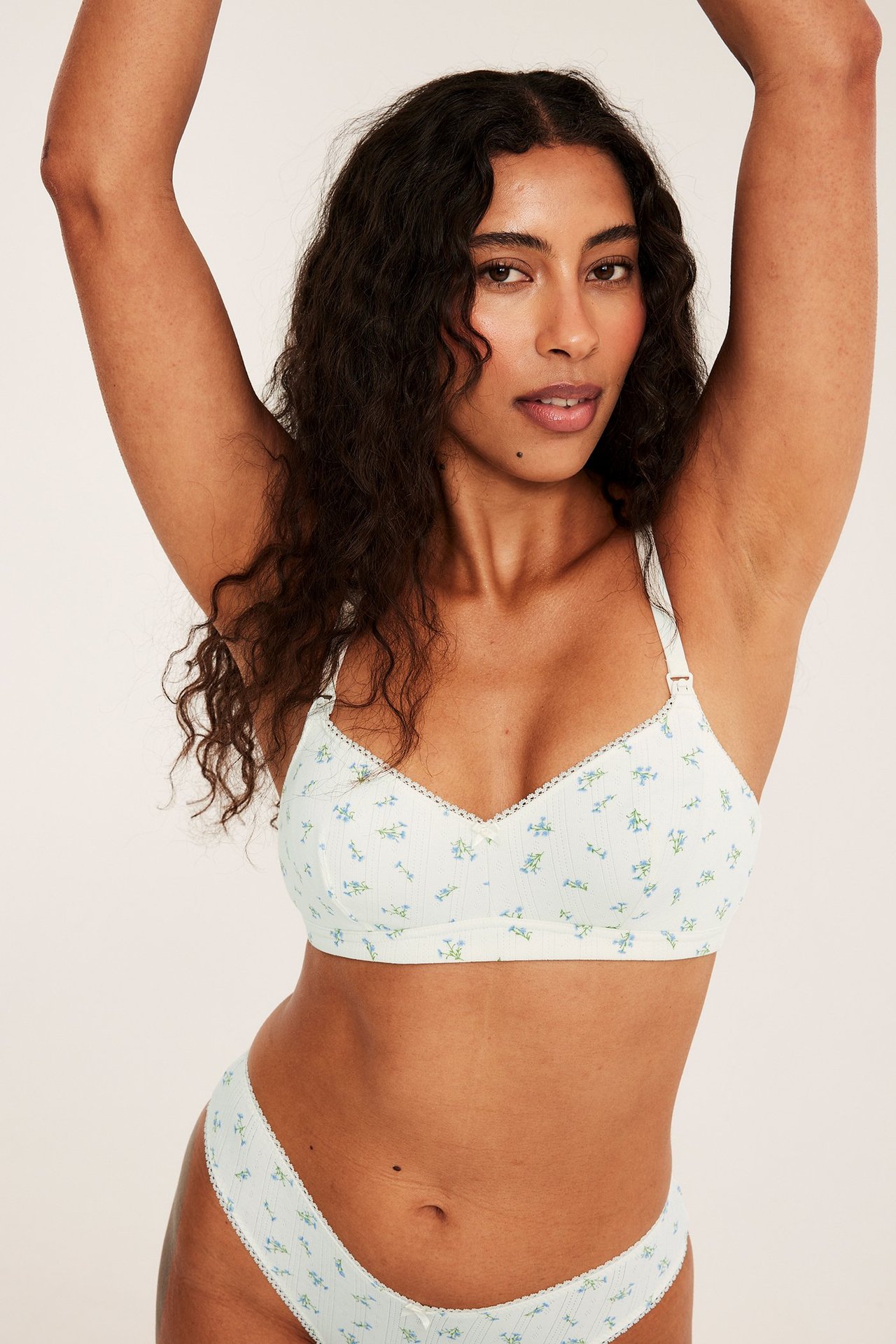 Framifrån en kvinna i offwhite pointelle amnings-bh med ljusblått blommigt tryck och matchande trosor.