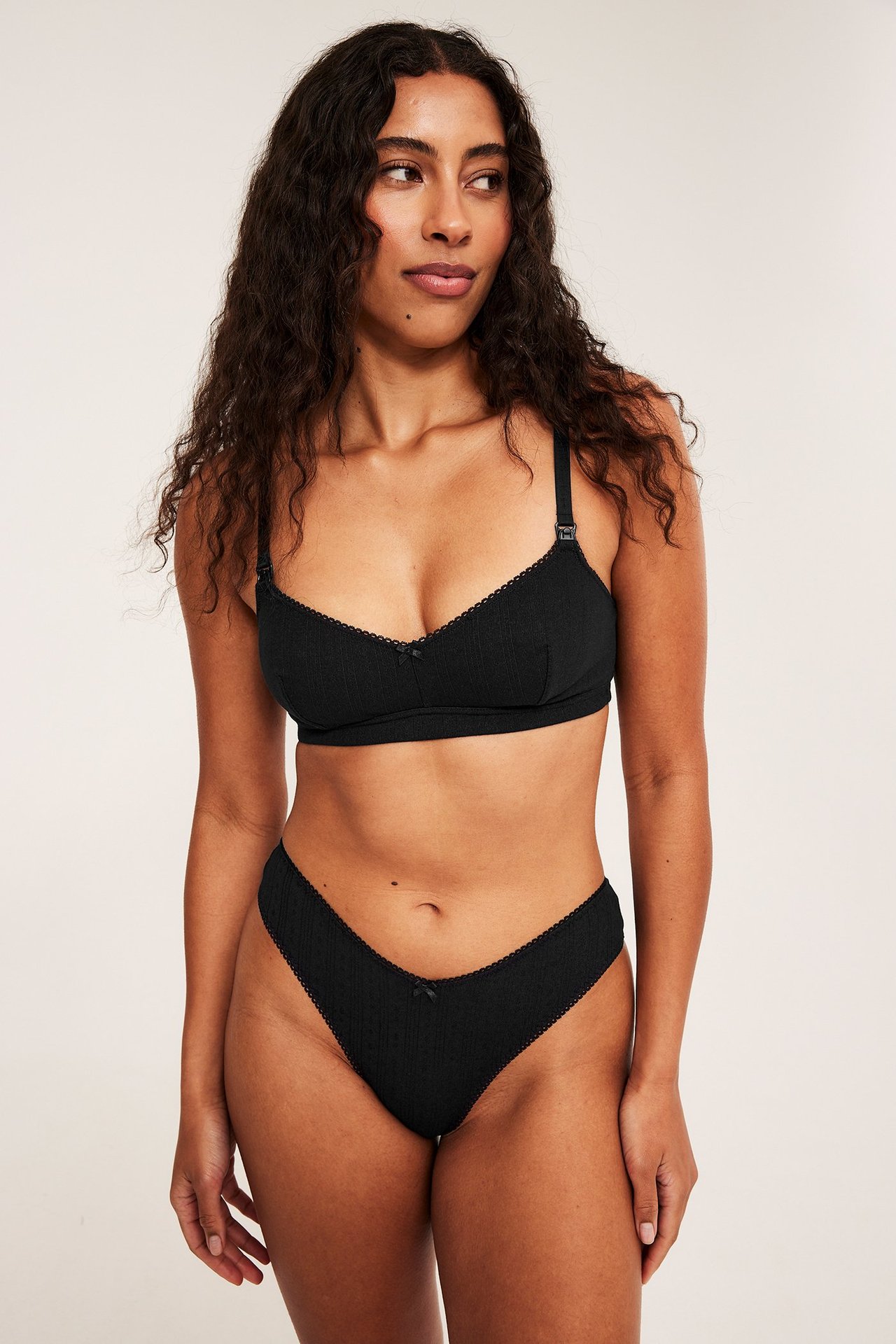 Framsida av kvinna i svart pointelle-ribbad amnings-bh med picotkant och matchande trosa.