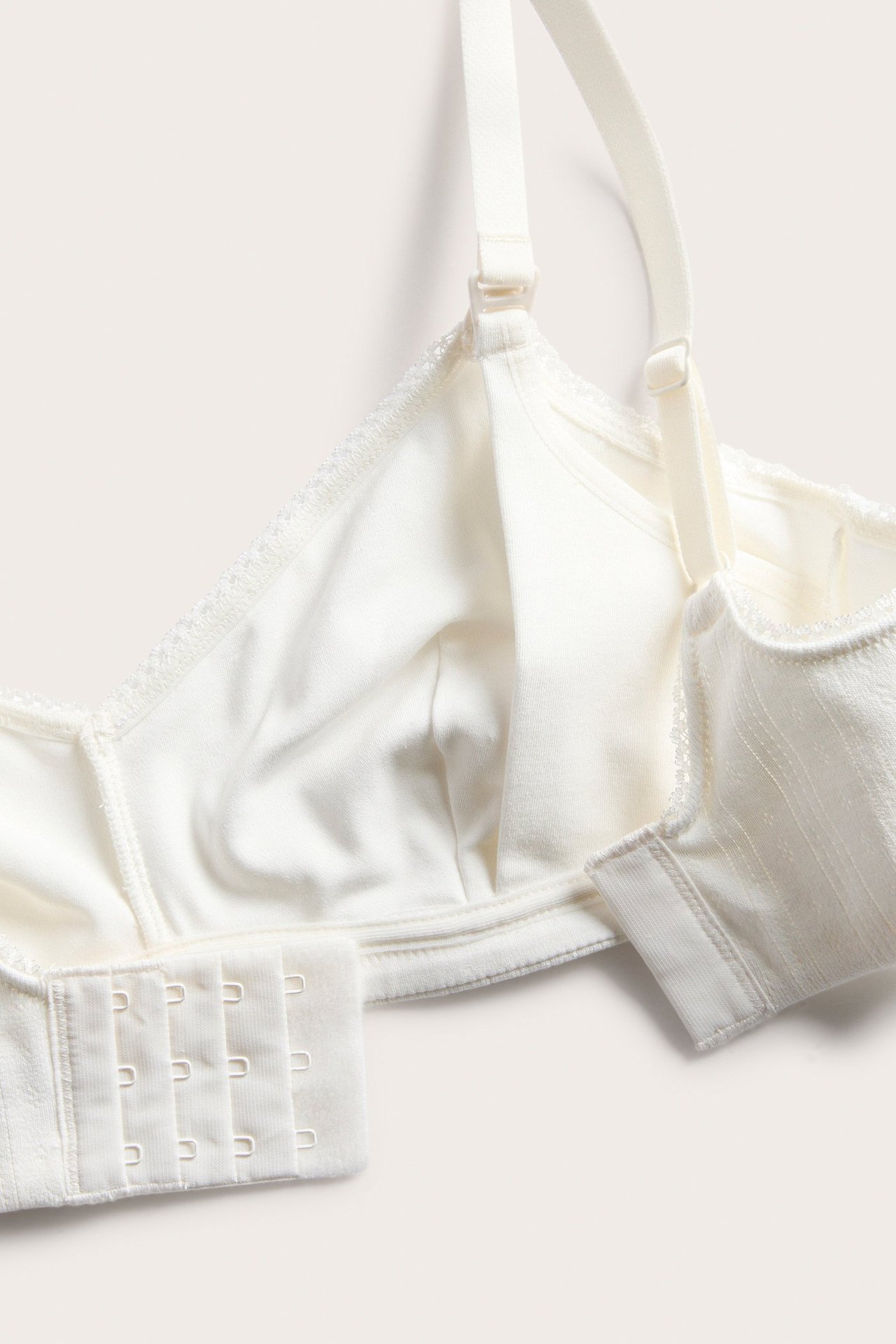 Lähikuva luonnonvalkoisista imetysliiveistä, pointelle-ribbiä, säädettävät olkaimet ja hakaskiinnitys.