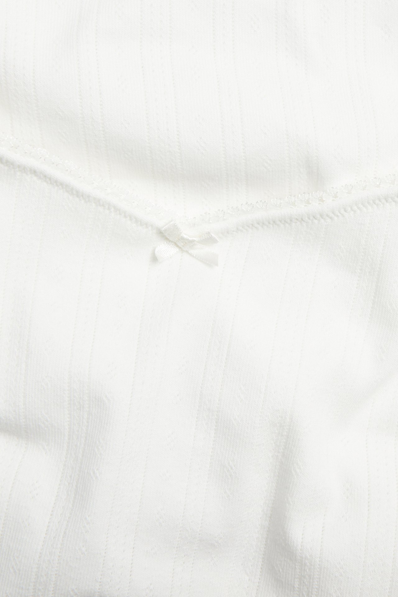 Zbliżenie na śmietankową koszulkę do karmienia z dzianiny pointelle, z elastyczną lamówką picot i kokardką.