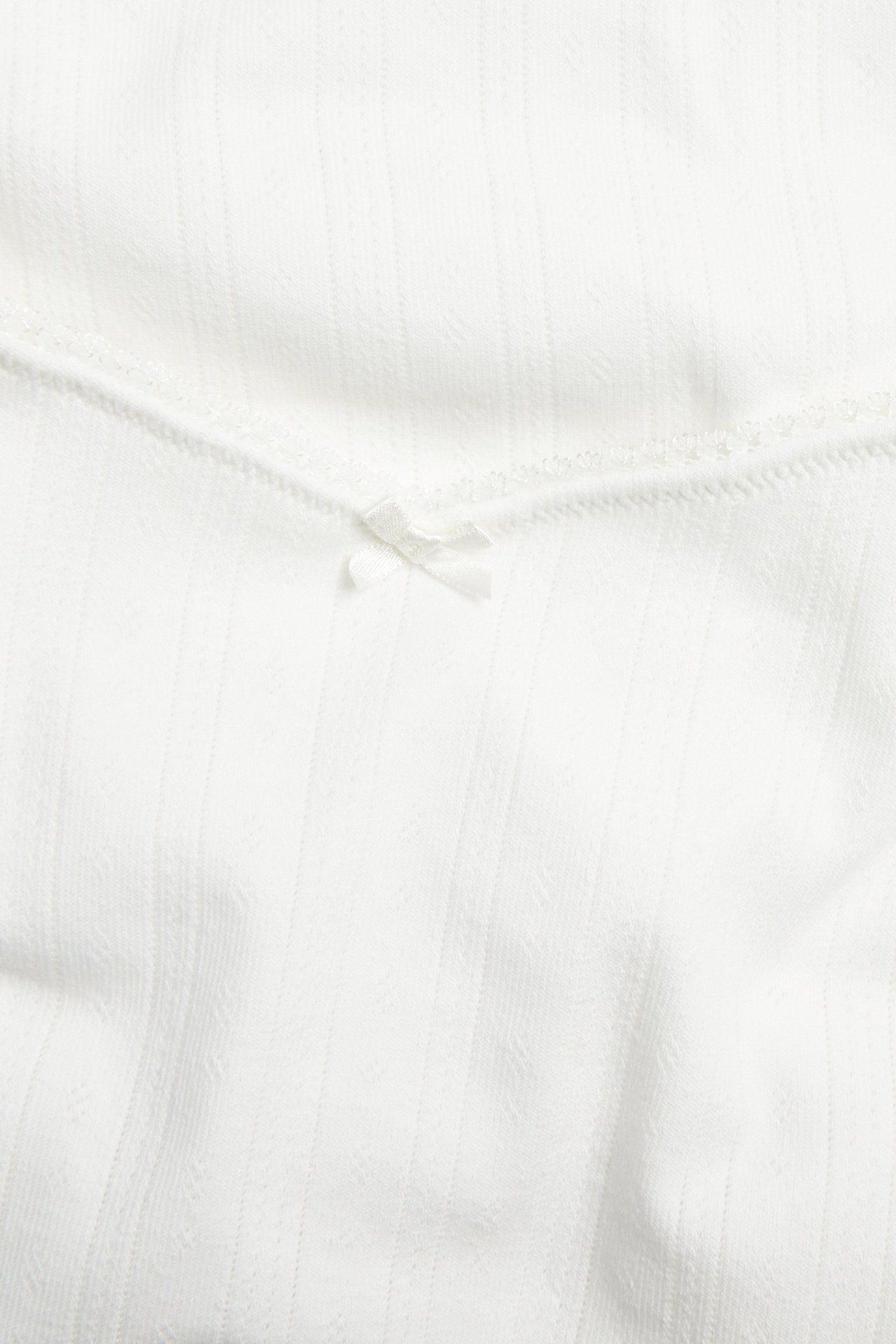 Lähikuva luonnonvalkoisesta pointelle-ribbineuloksesta imetystopista, jossa pikoresaari ja pieni rusetti.