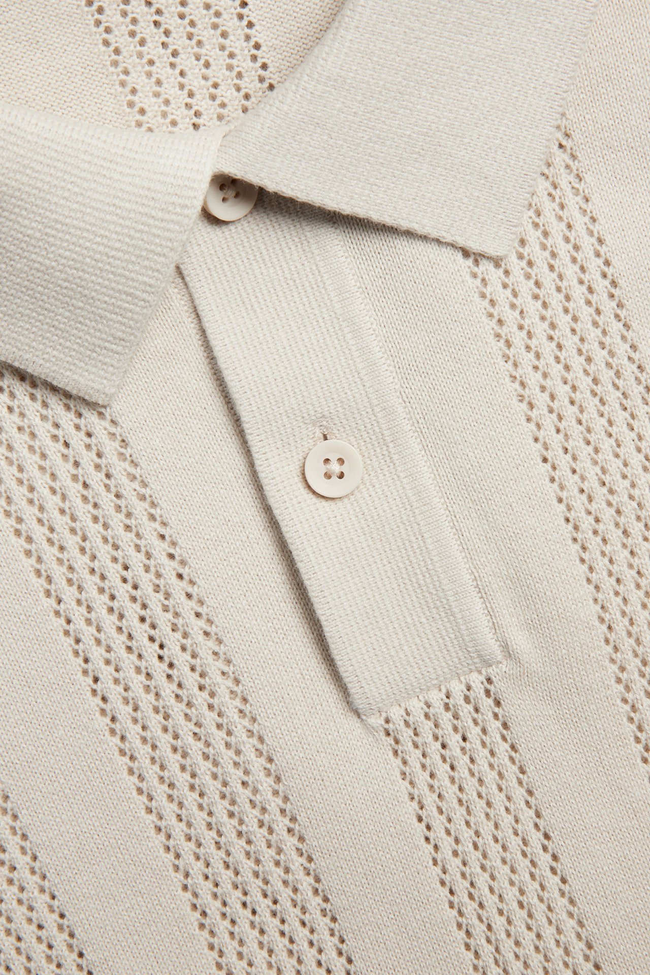 Nærbilde av en lys beige strikket piké med strukturmønster og to knapper.