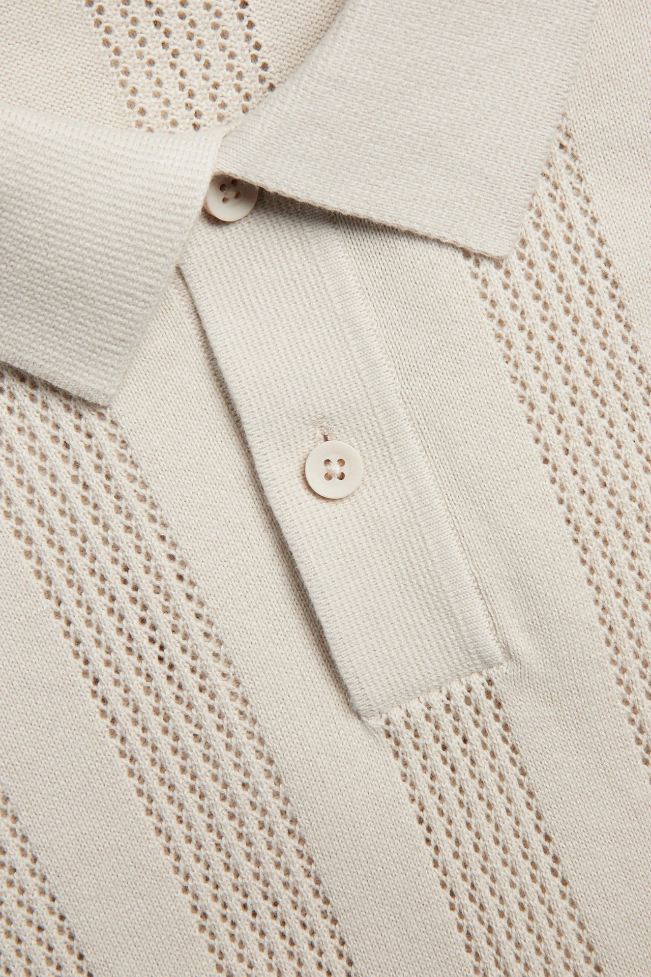 Zbliżenie beżowej dzianinowej koszulki polo ze strukturalnym wzorem i dwoma guzikami.