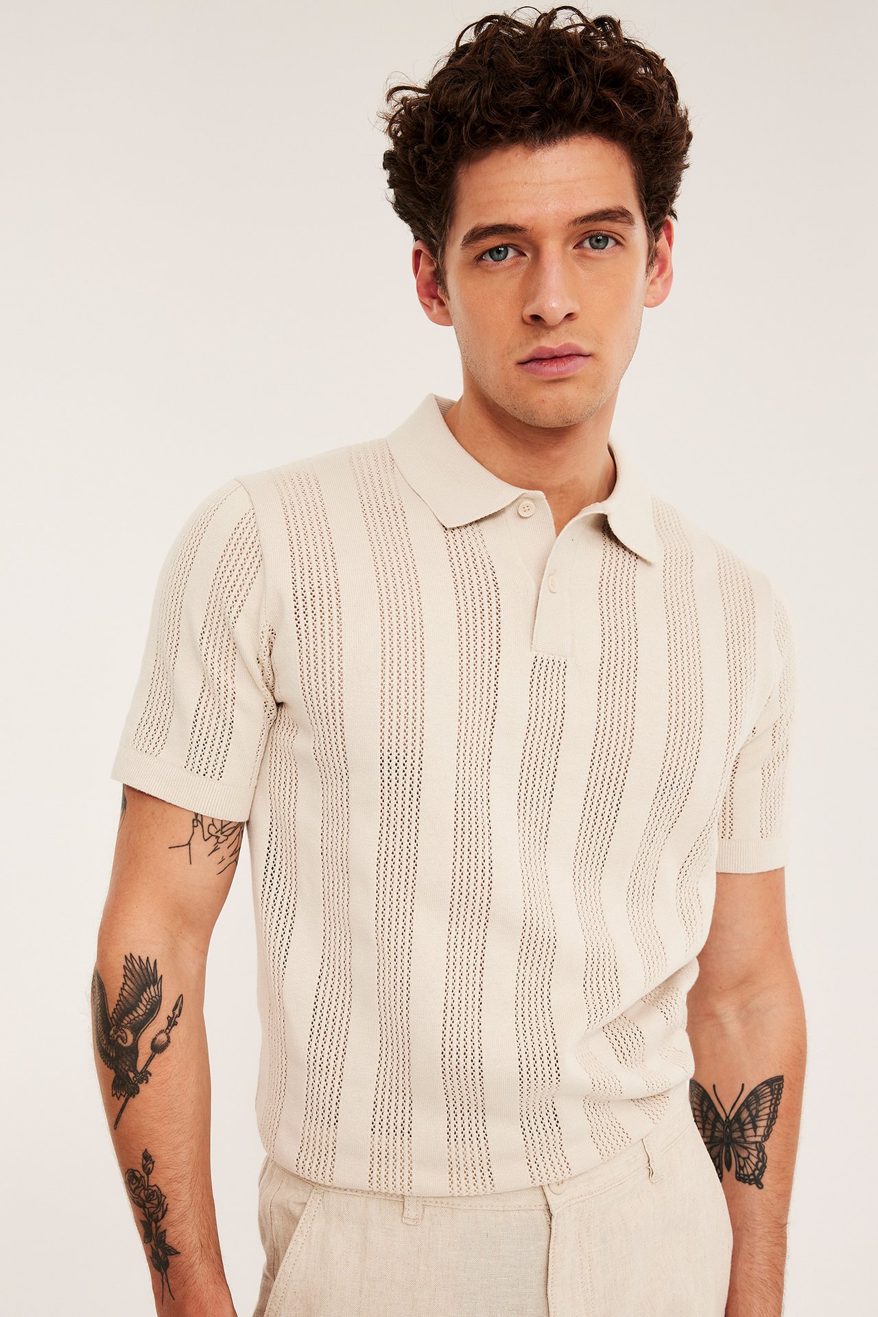 Frontbilde: Mann i en lys beige kortermet strikket poloskjorte med stripemønster, to knapper og beige bukser.