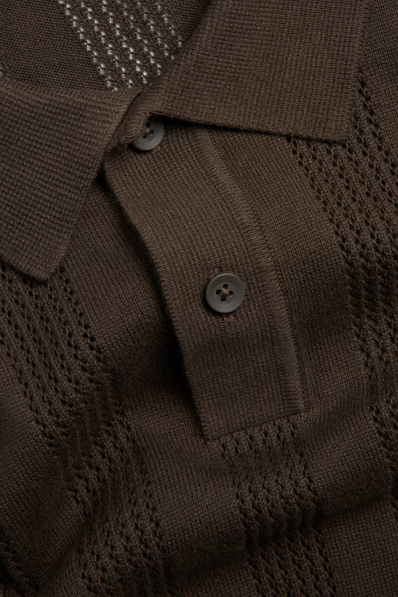 Nærbilde forfra av en brun kortermet strikket pikétrøye med strukturmønster og to knapper.
