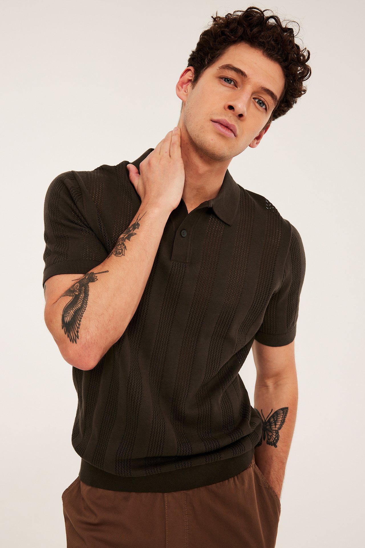 Framifrån, man i en brun stickad kortärmad pikétröja med strukturmönster och bruna byxor.