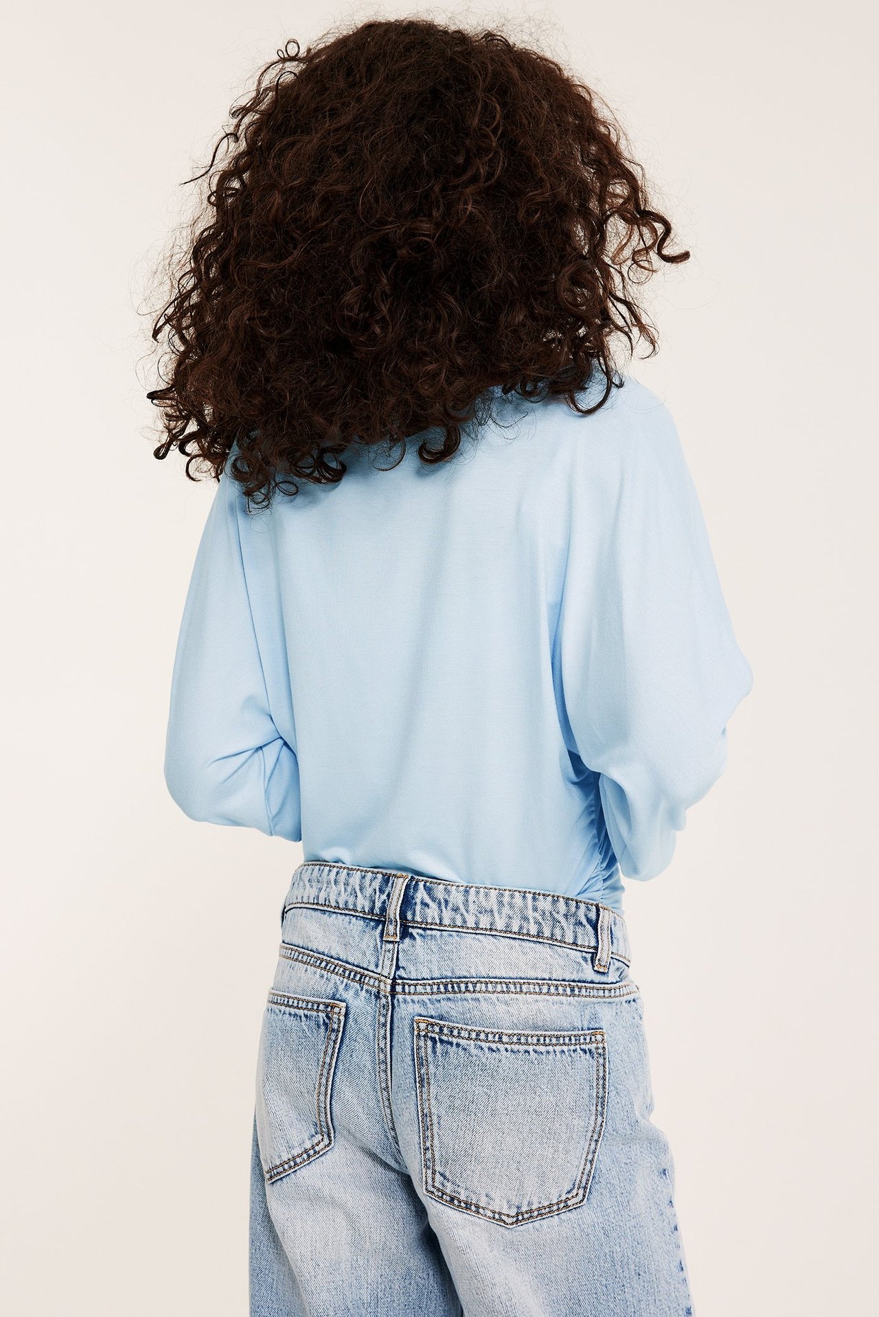 Ryggvy av ett barn i ljusblå långärmad topp med puffärmar och ljusa jeans.