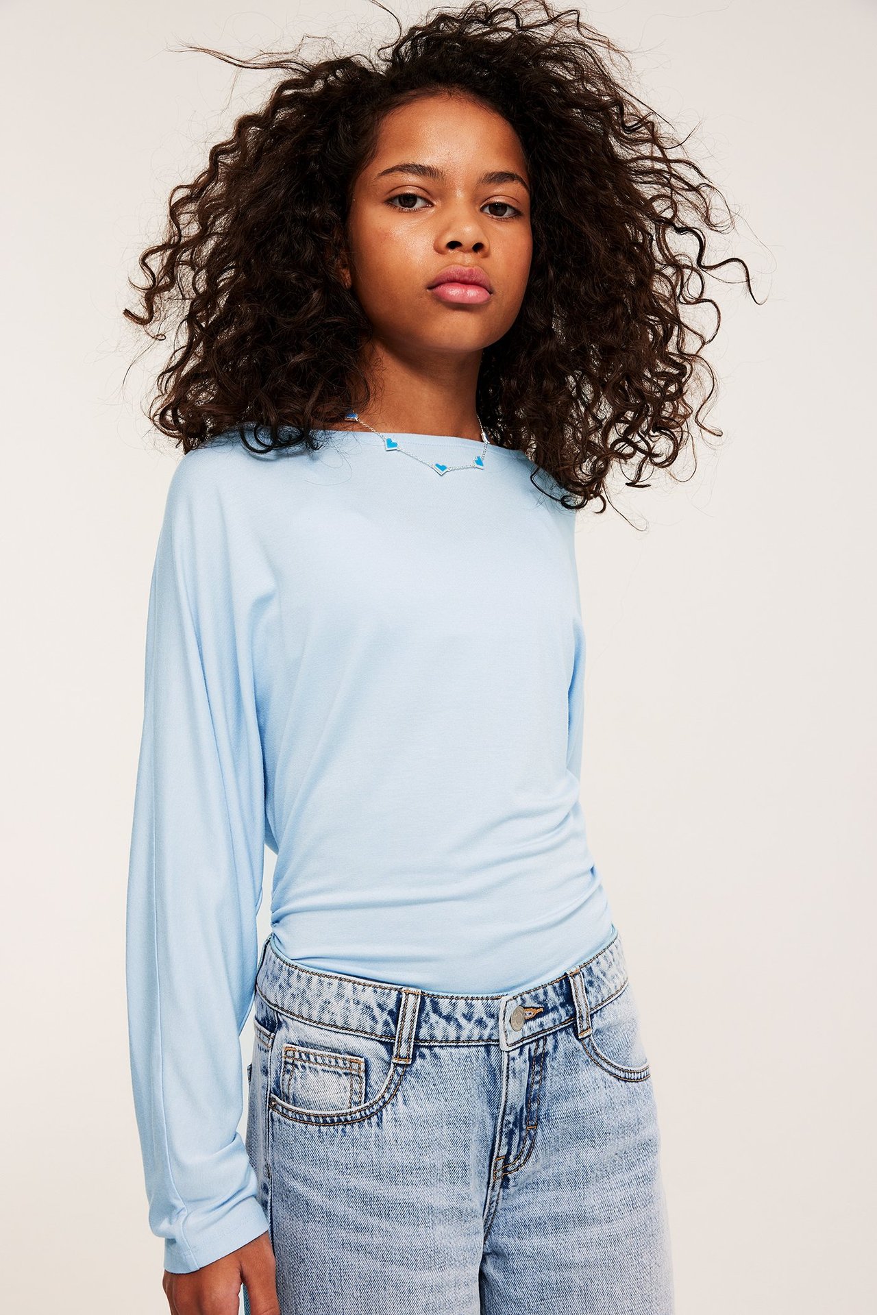 Frontbilde av et barn i lyseblå langermet topp, lyseblå jeans og et halskjede med blå hjerter.