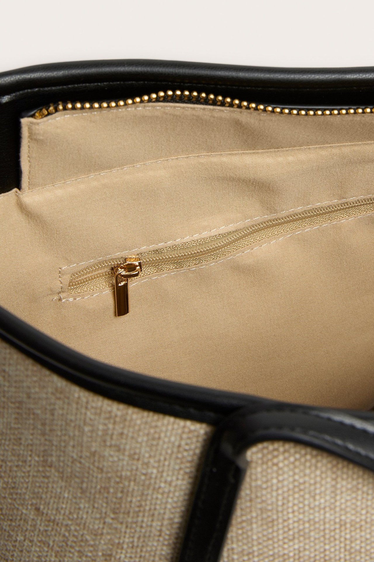 Lähikuva beigestä olkilook-kassista, jossa musta reunus, vaalea vuori ja sisävetoketjutasku.