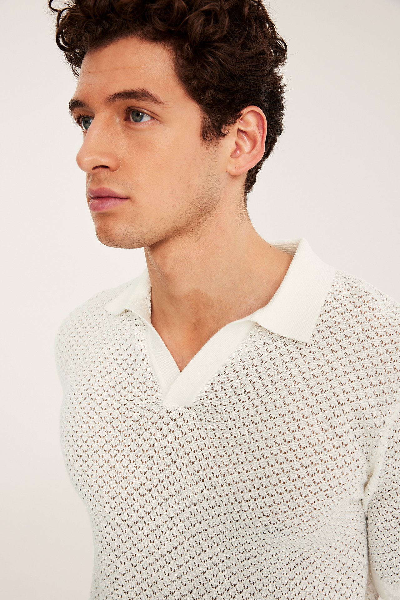 Närbild i sidoprofil på man i offwhite hålstickad kortärmad pikétröja.