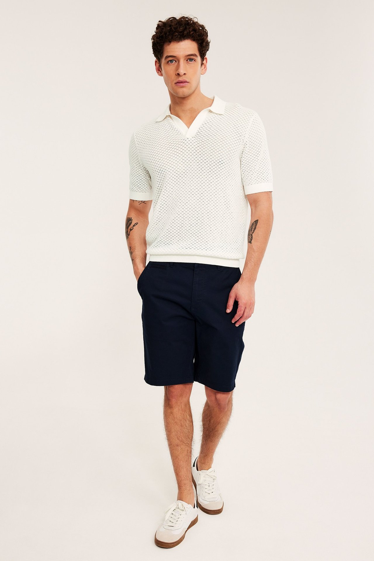 Forfra: mann i offwhite hullstrikket kortermet piké, marineblå shorts og hvite joggesko.