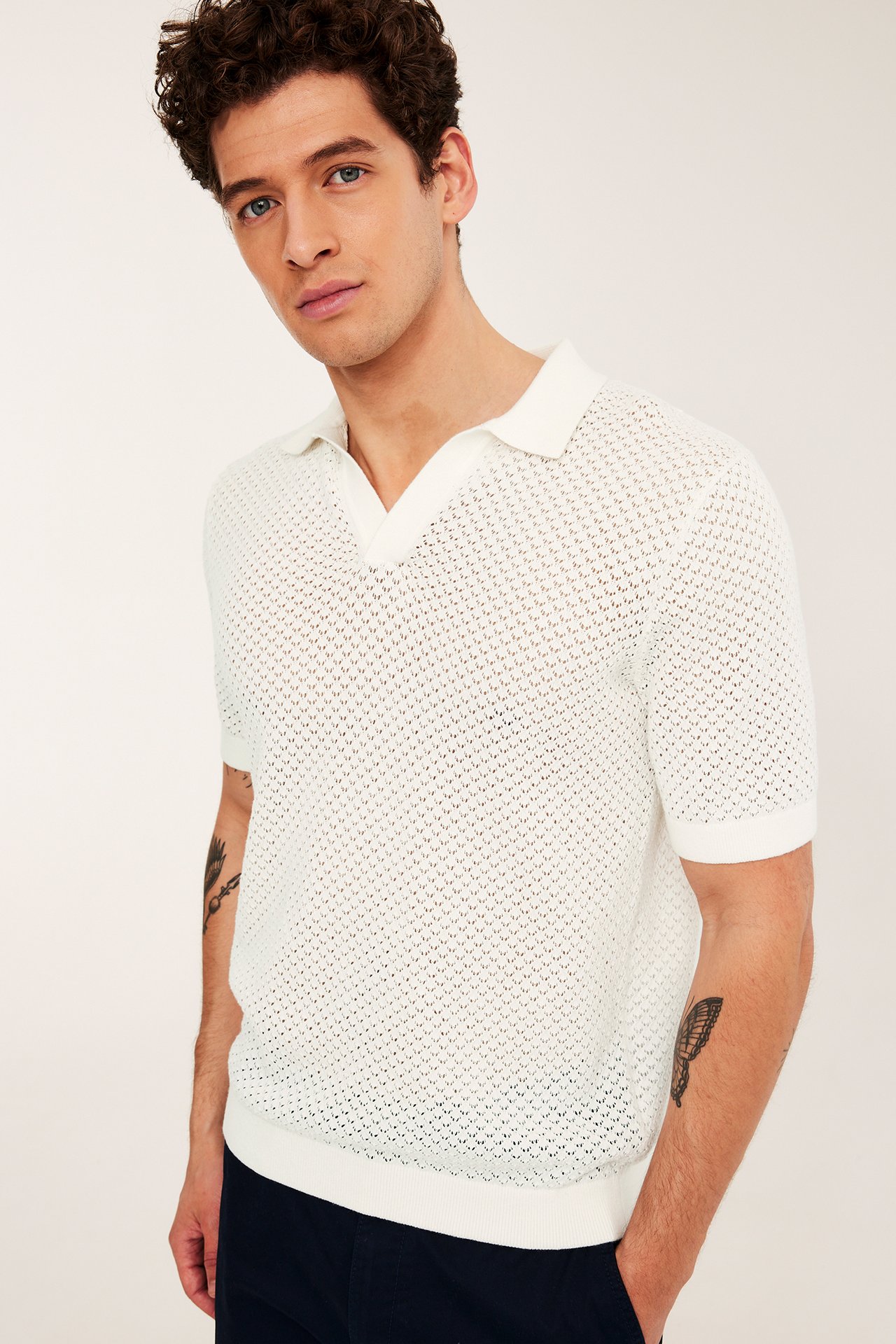 Forfra: mann i offwhite hullstrikket kortermet poloskjorte med mønster og mørkeblå bukser.