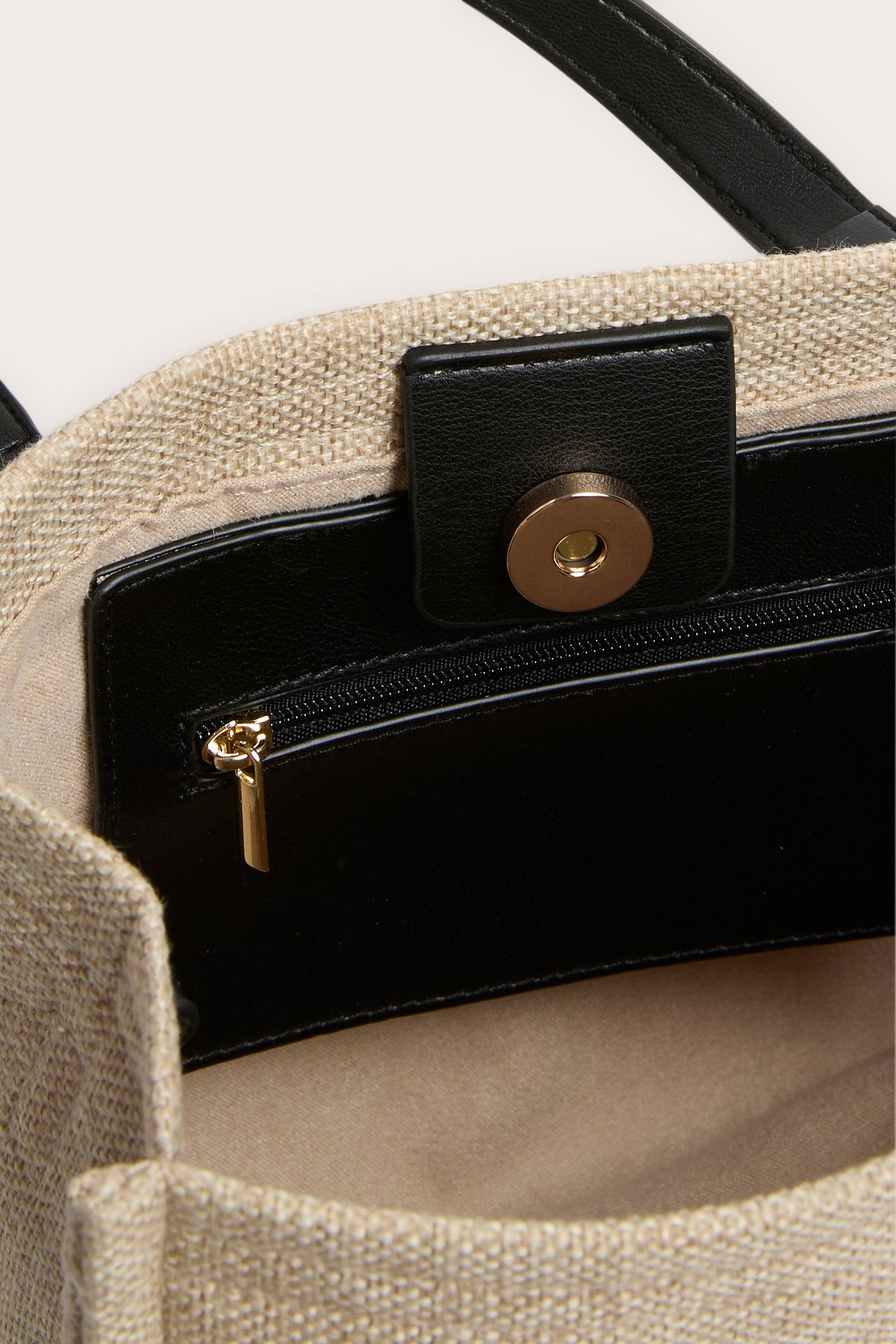 Ylhäältä näkymä beigestä kangaskassista, jossa on musta reunus, magneettisuljin ja sisävetoketjutasku.