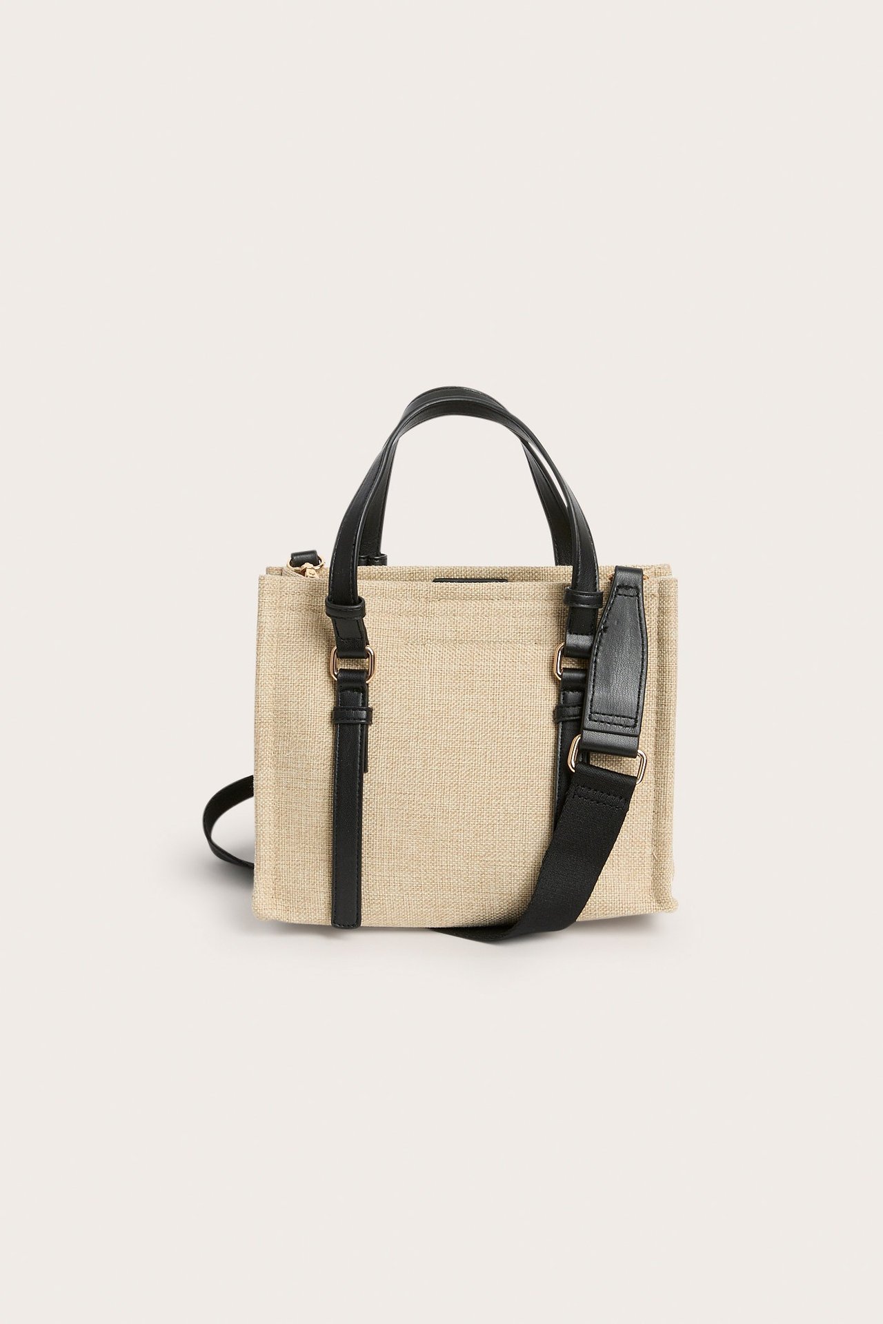 Edestä näkymä: Beige kangasminitote-laukku mustilla yläkahvoilla ja säädettävällä mustalla olkahihnalla.
