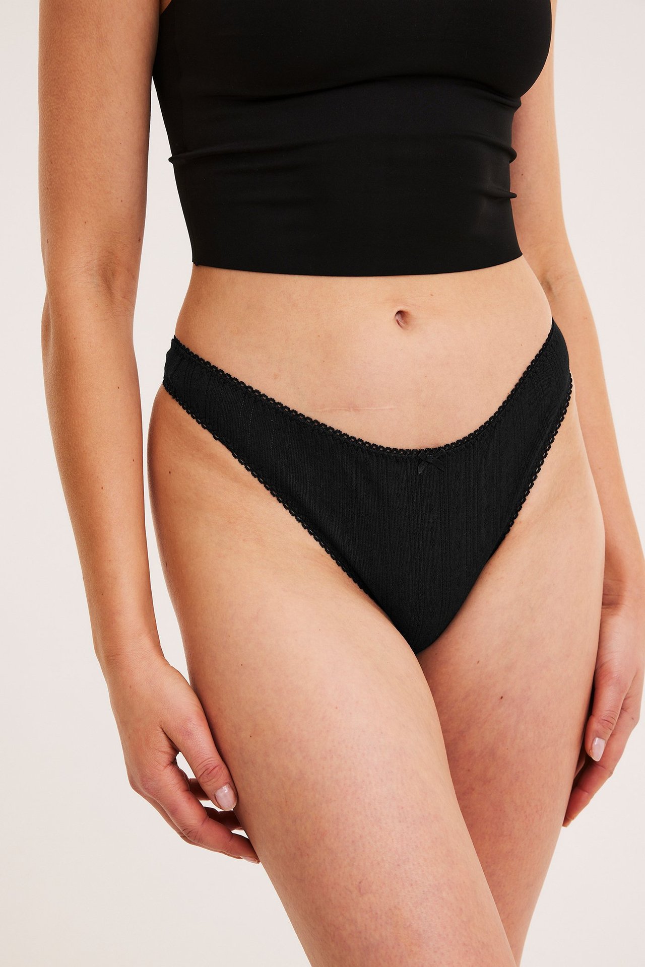 Etunäkymä naisesta, jolla on mustat pointelle-stringit pitsireunuksella ja musta crop top.