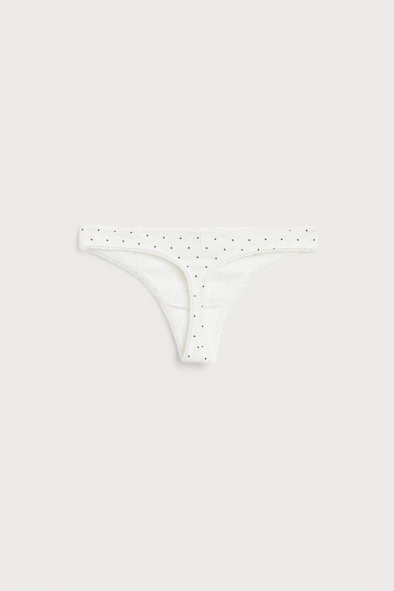 Forfra, offwhite pointelle stringtruse med små svarte prikker.
