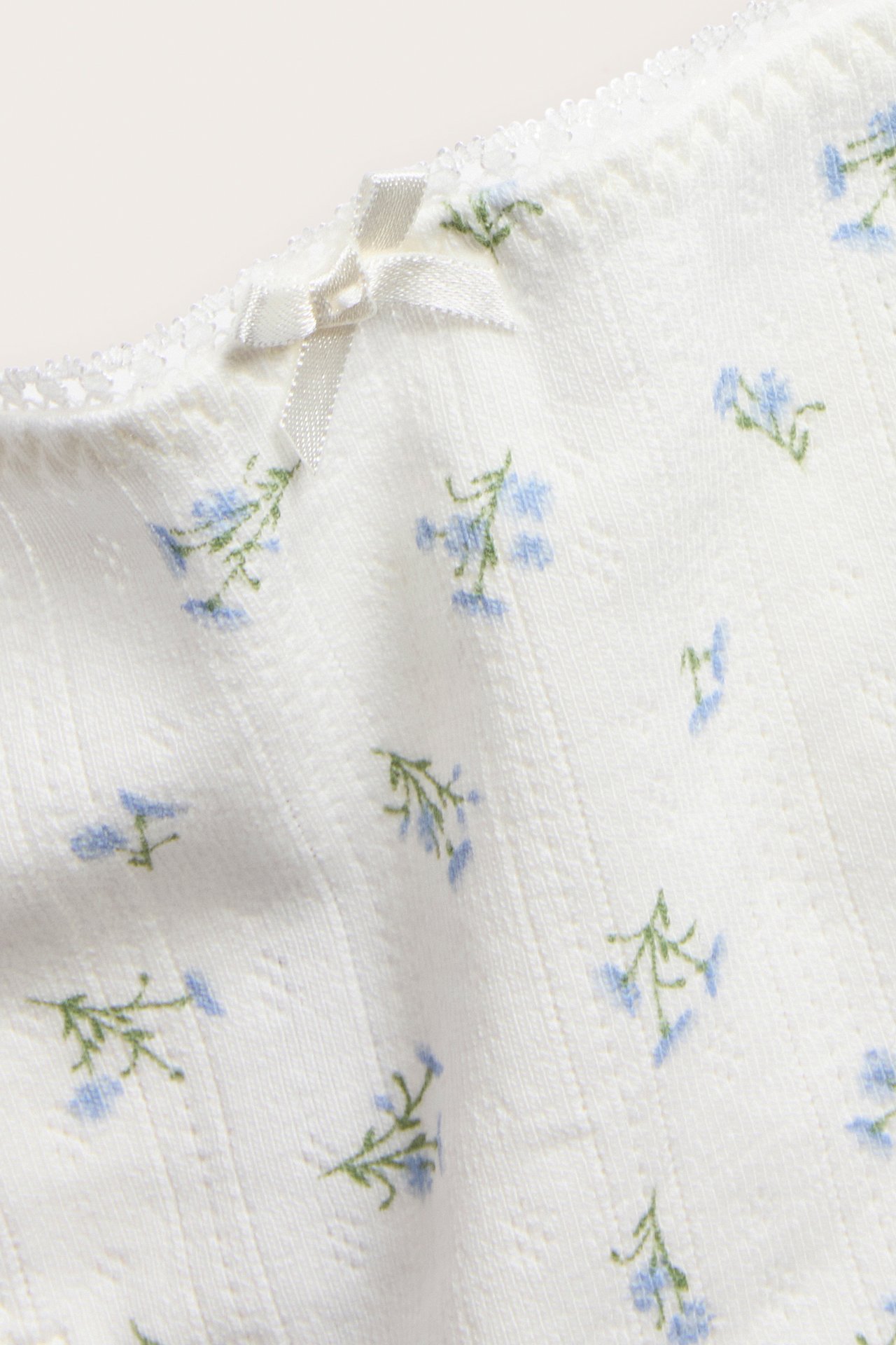 Nærbilde av offwhite pointelle stringtruse med blått blomstermønster, liten sløyfe og blondekant.