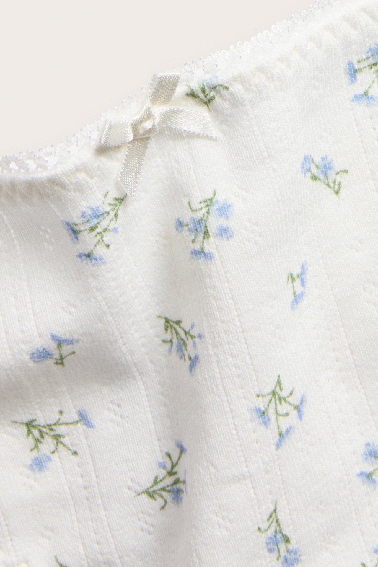 Nærbilde av offwhite pointelle stringtruse med blått blomstermønster, liten sløyfe og blondekant.