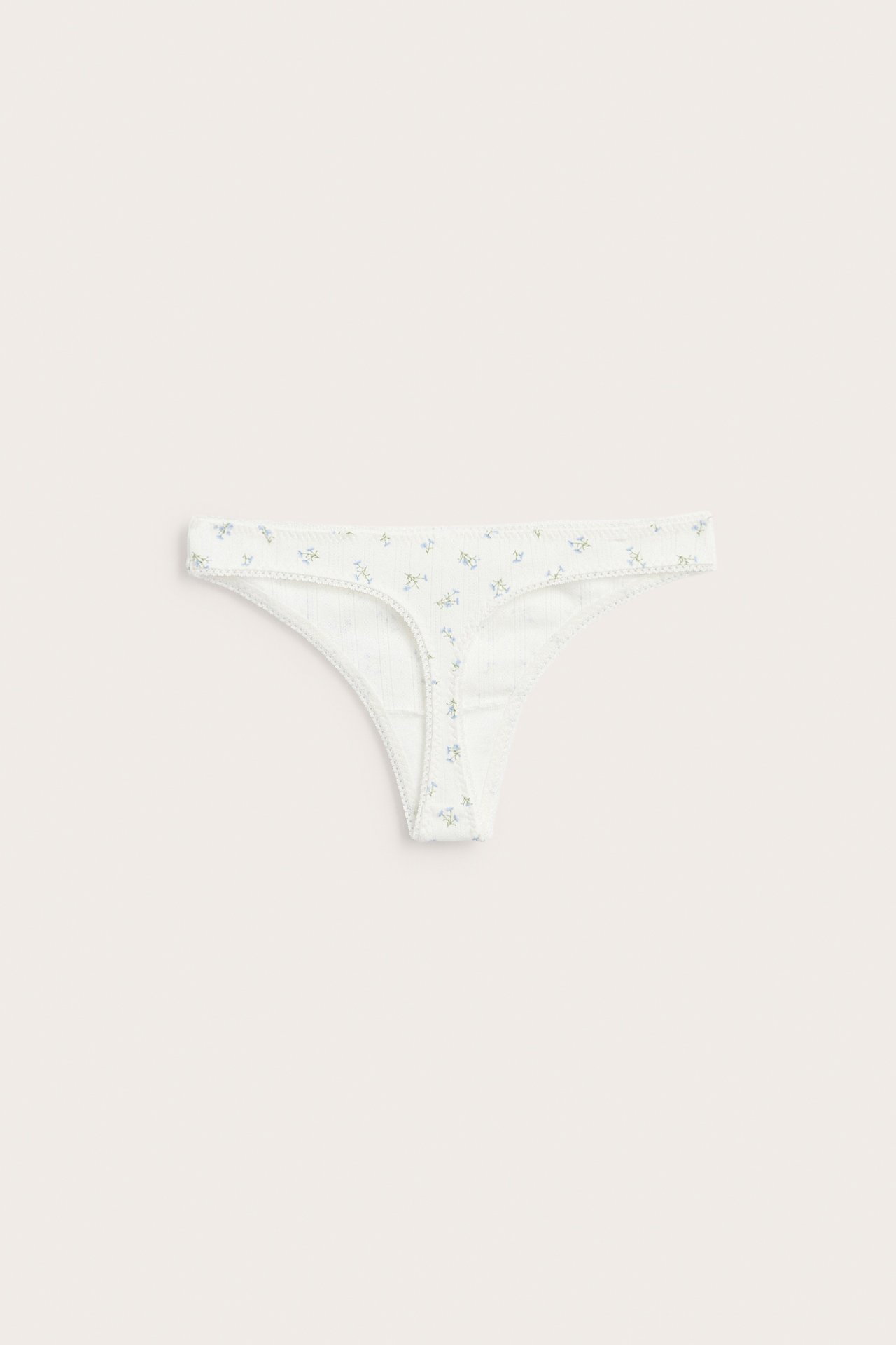 Frontvisning av offwhite pointelle stringtruse med blomstermønster, flatlagt.