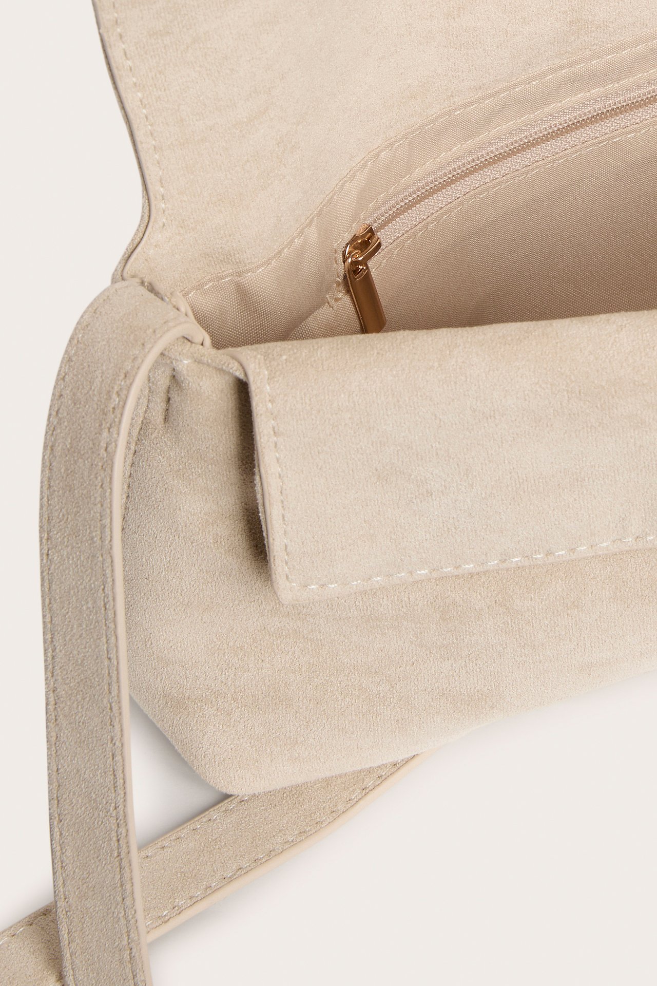 Närbild på ljusbeige axelremsväska i mockaimitation, med öppen flik som visar en invändig dragkedjeficka.