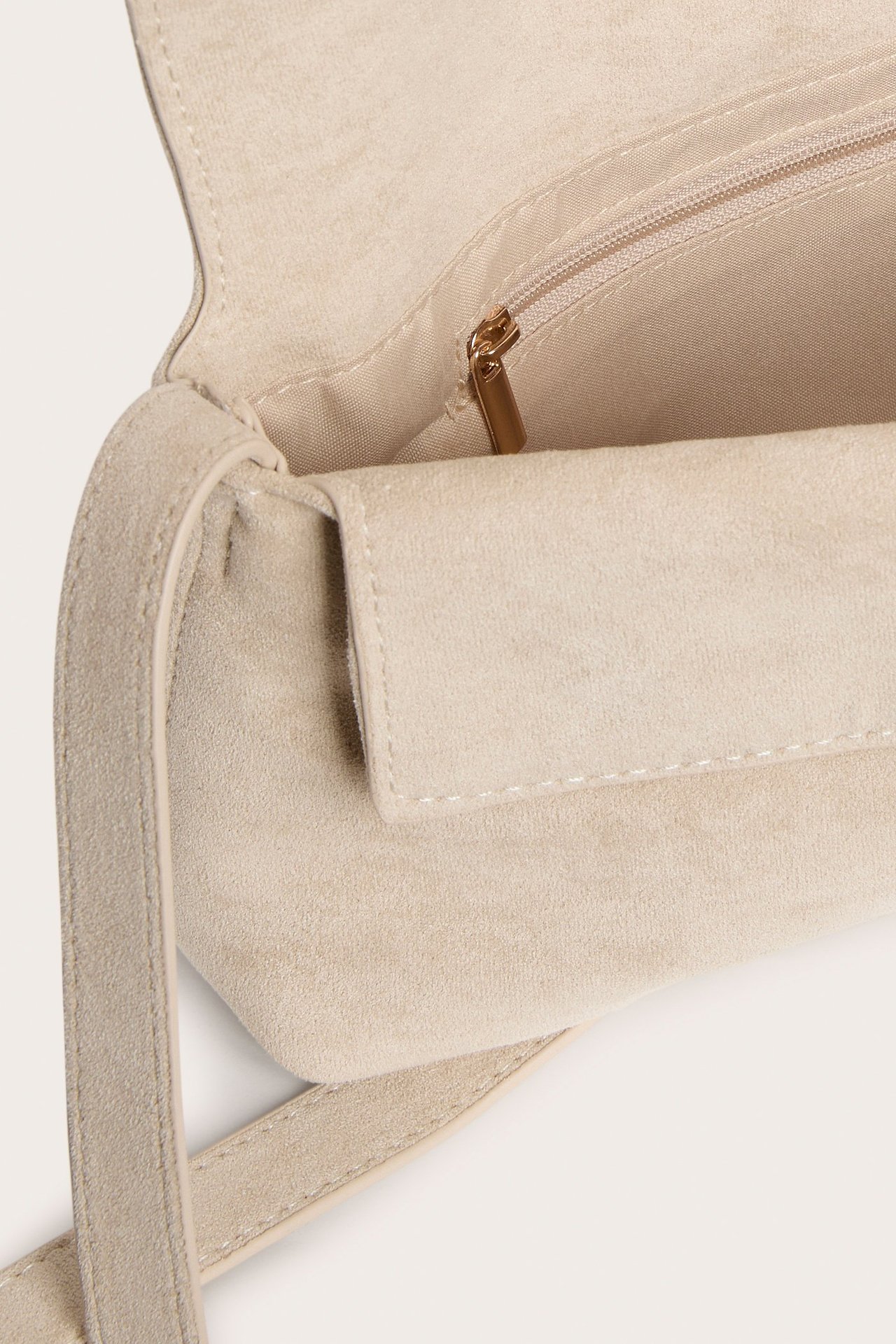 Närbild på ljusbeige axelremsväska i mockaimitation, med öppen flik som visar en invändig dragkedjeficka.