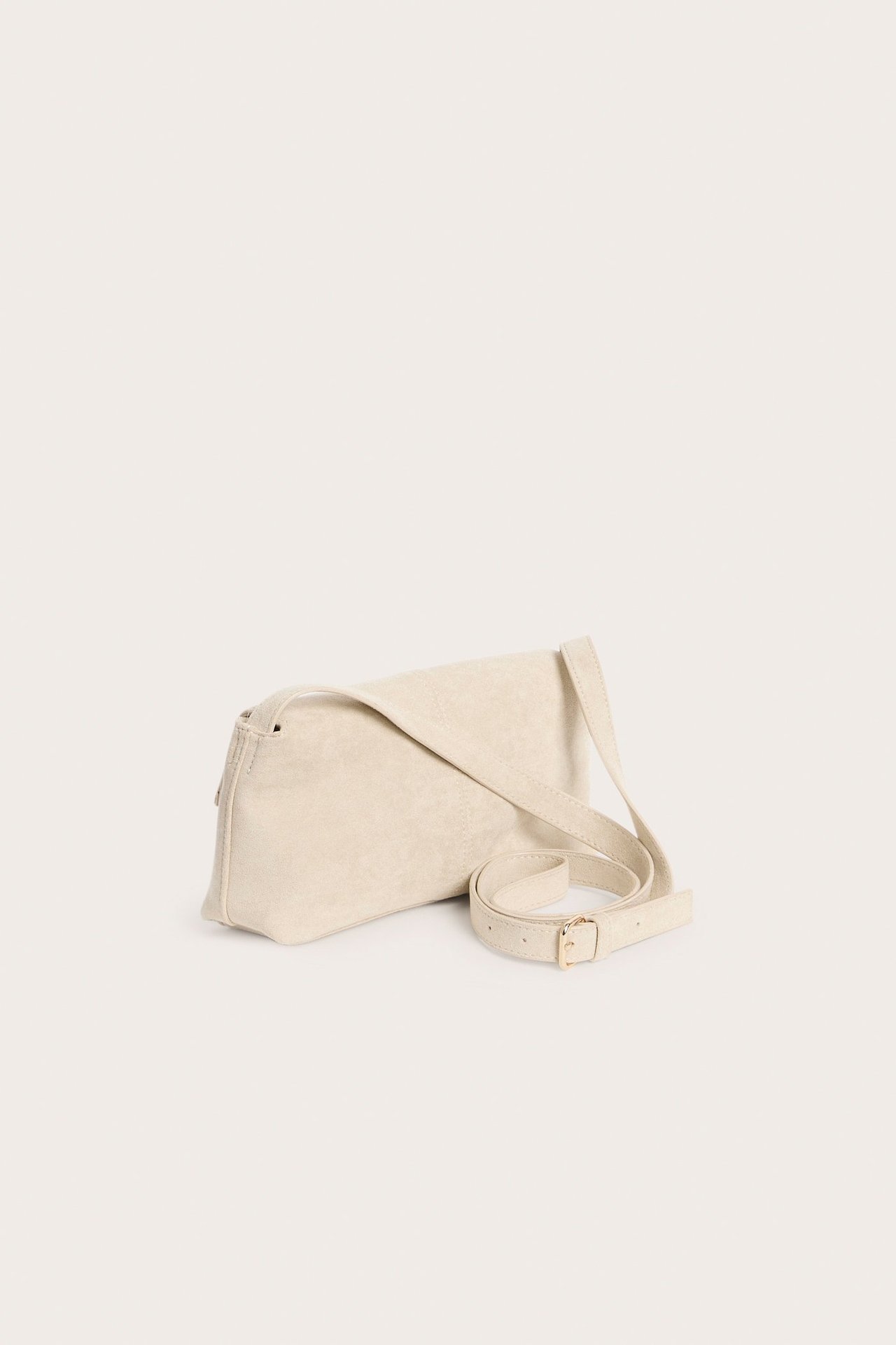 Sidovy av en ljusbeige axelremsväska i mockaimitation med lång rem och magnetlås.