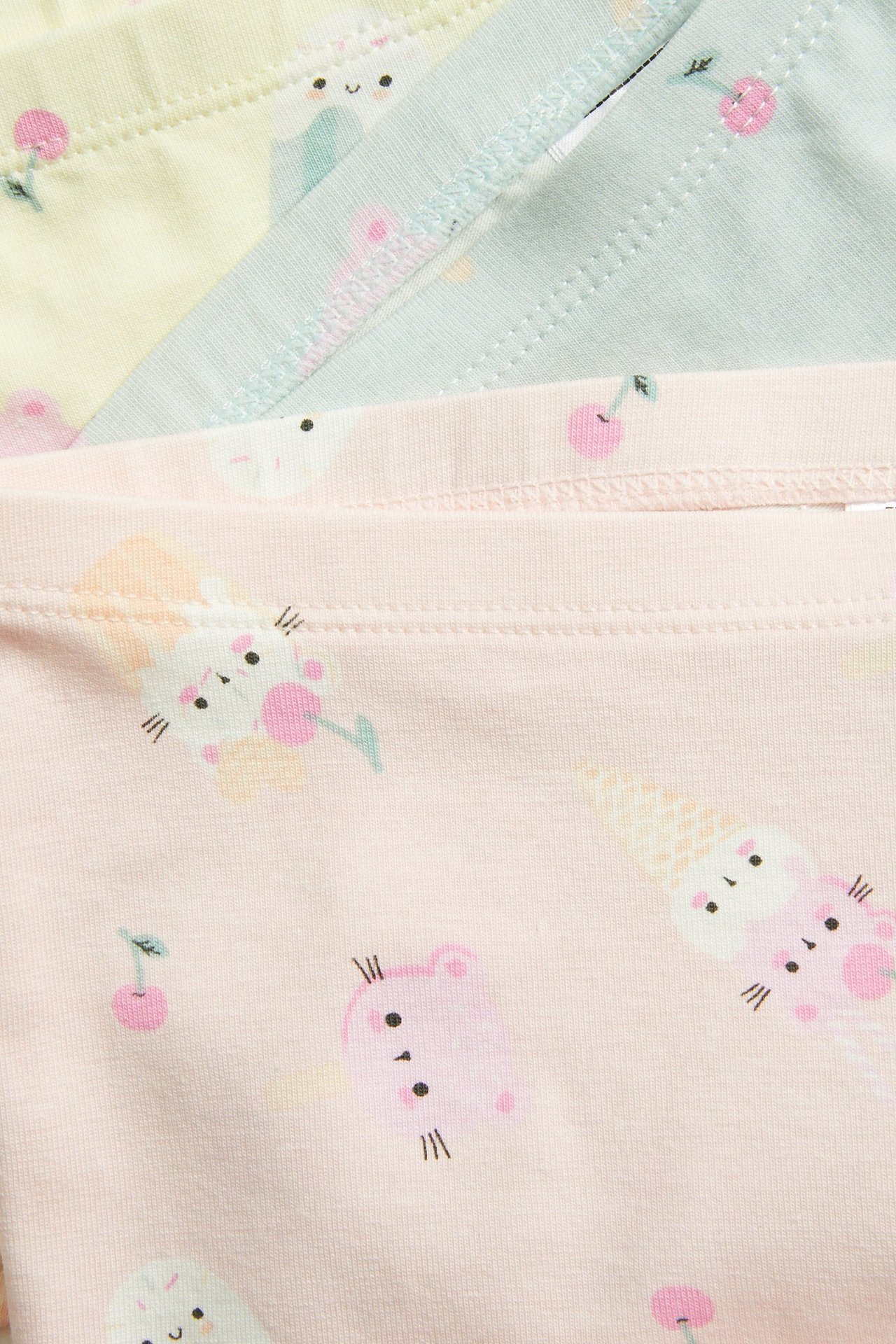 Lähikuva kolmesta lasten kuvioidusta puuvillabokserista vaaleanpunaisena, sinisenä ja keltaisena jäätelökuviolla.