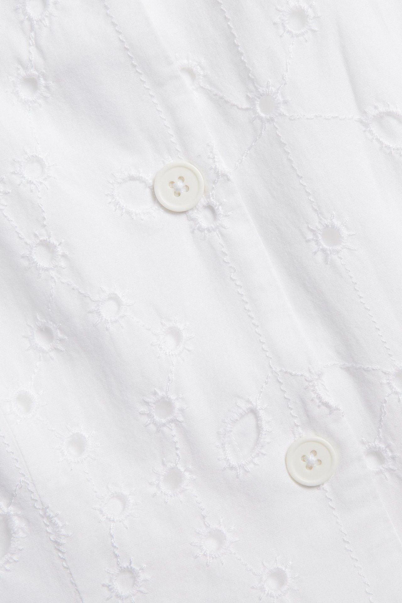 Nærbilde av en hvit bomullsvest med broderie anglaise og knapping foran.