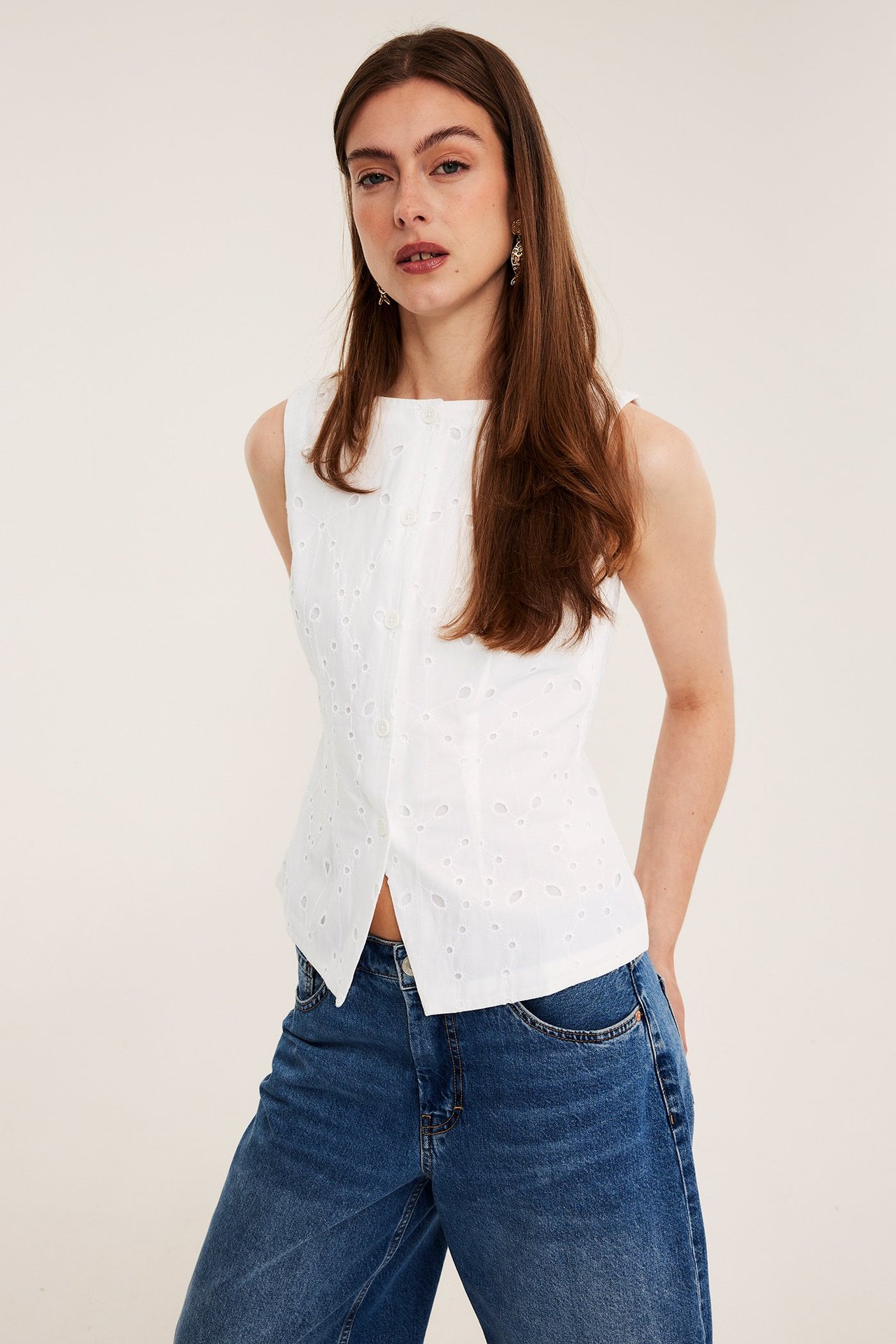 Edestä, nainen yllään valkoinen puuvillainen broderie anglaise -liivi napeilla ja siniset, leveälahkeiset farkut.