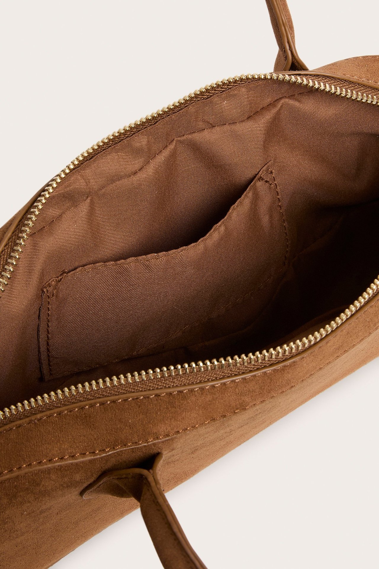 Närbild, uppifrån av öppen brun mockaimitation handväska med dragkedja och brunt polyesterfoder.