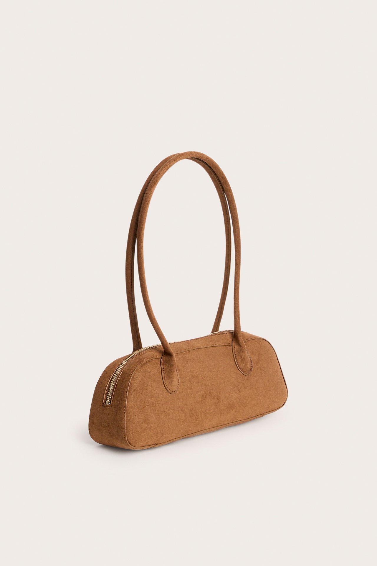 Front/sidevy av en brun handväska i mockaimitation, med två långa handtag och dragkedja.