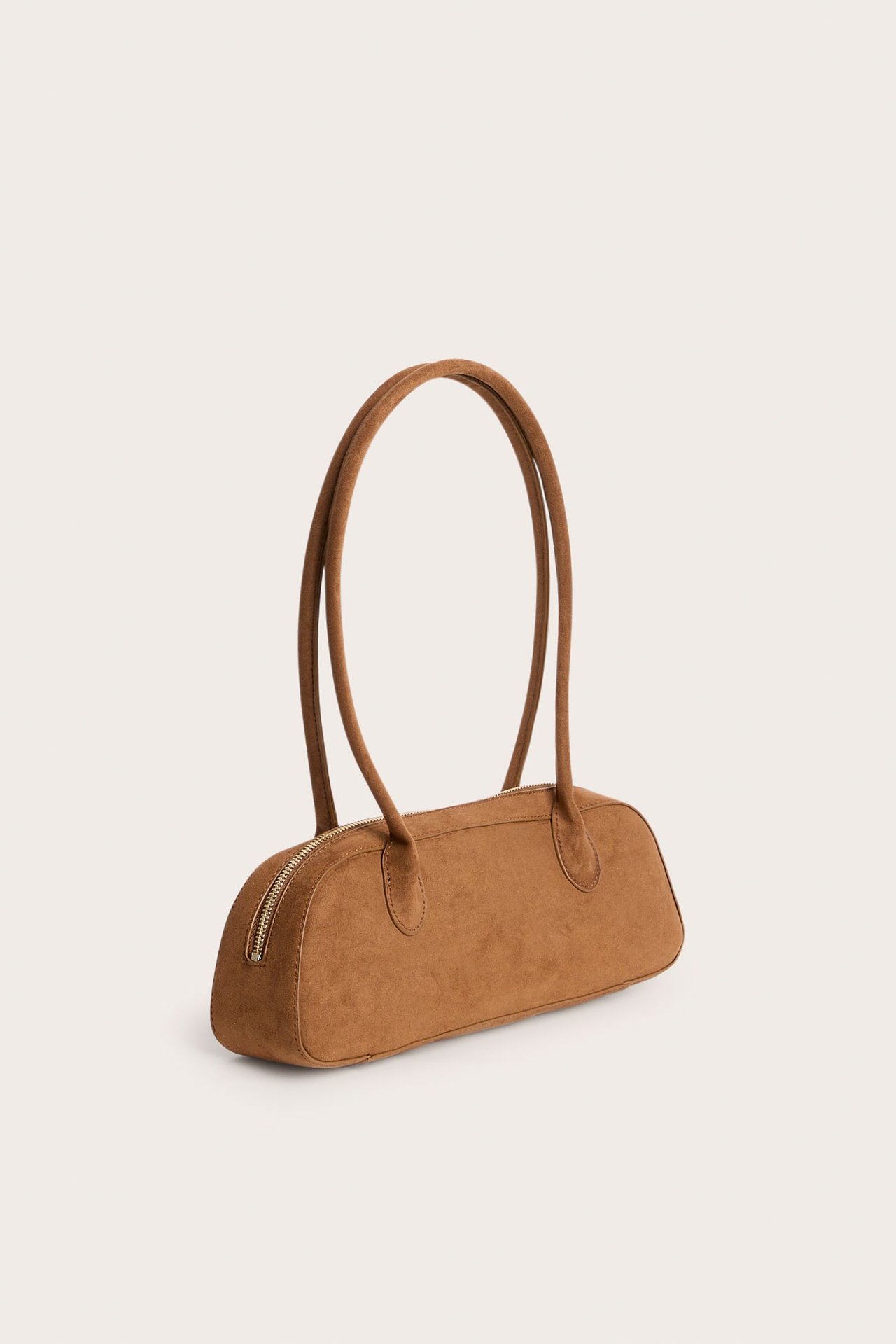 Front/sidevy av en brun handväska i mockaimitation, med två långa handtag och dragkedja.