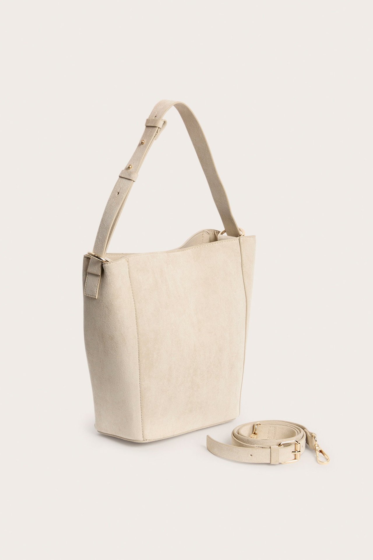 Trekvartsvisning av lys beige semsket skinnimitasjonsveske med justerbar rem og separat lang rem.