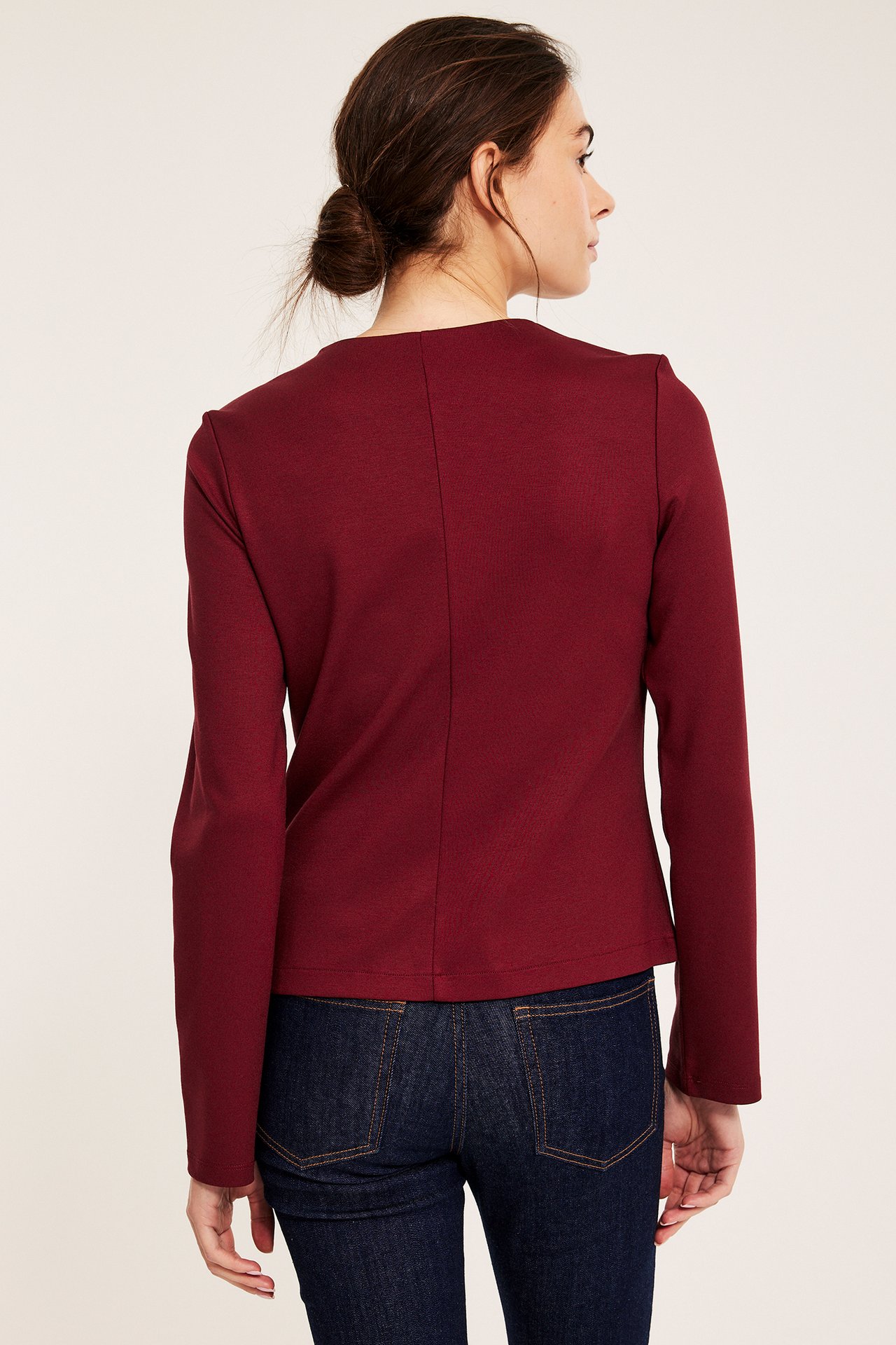 Naisen selkäkuva, yllään istuva punainen Punto jersey -takki ja tummansiniset farkut.