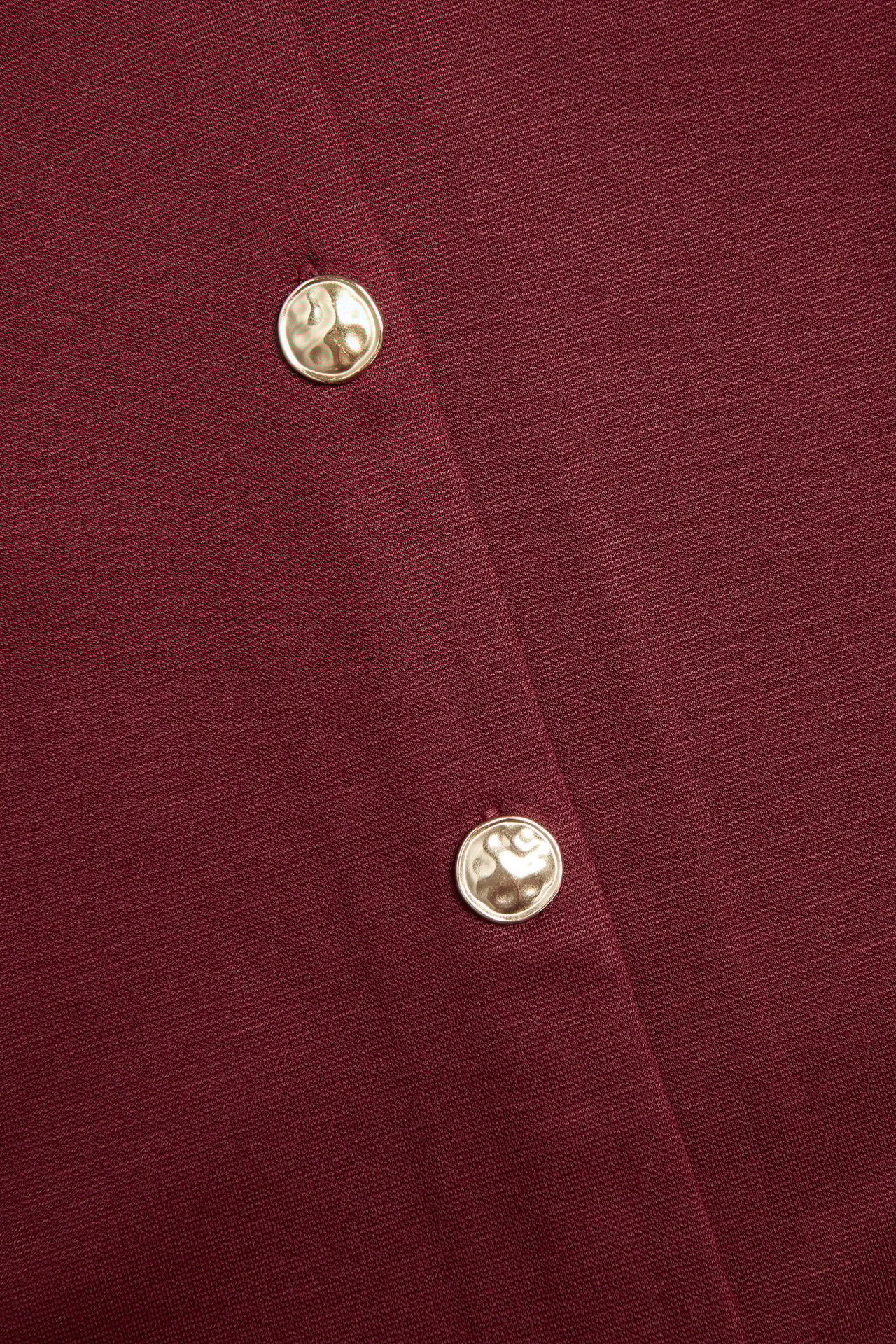 Zbliżenie czerwonego żakietu z dzianiny Punto z dwoma młotkowanymi złotymi guzikami.