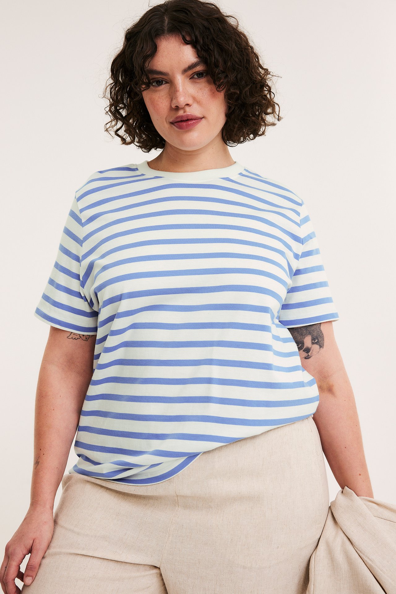 Framifrån, en kvinna i avslappnad ljusblå och benvitrandig t-shirt och beiga byxor.