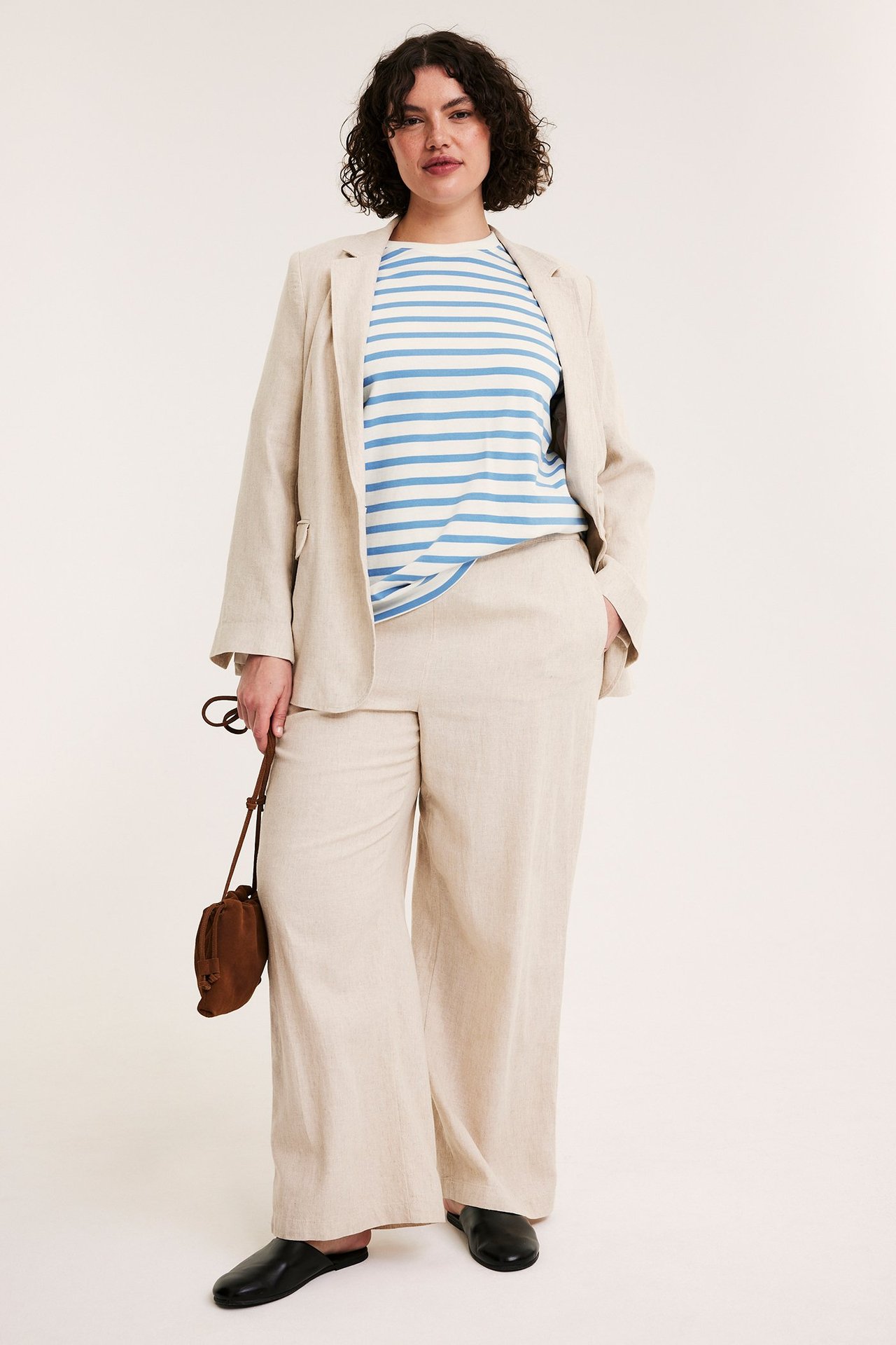 Front view: Kvinna i blåvitrandig bomulls-t-shirt, beige linnekostym, svarta mules, med brun väska.