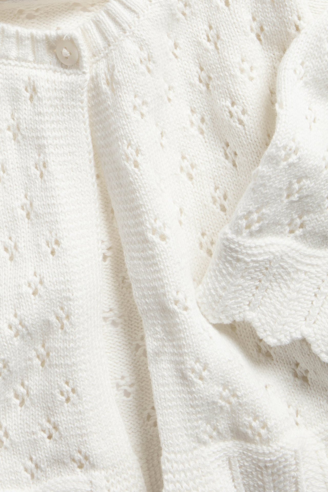 Zbliżenie na kremowy, wzorzysty bawełniany sweter rozpinany z guzikiem i falbanowymi brzegami.