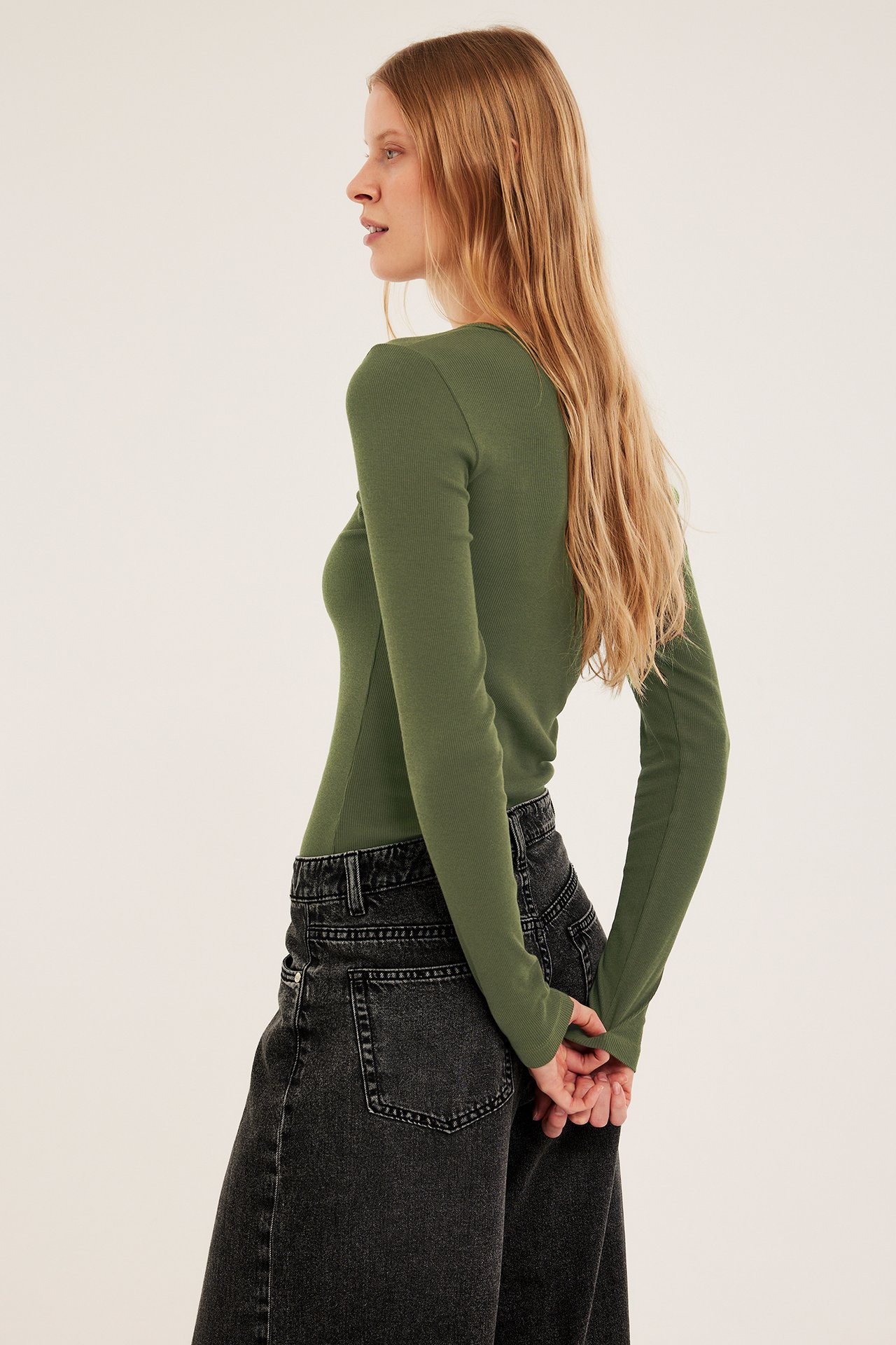 Naisen sivukuva yllään khakinvihreä ribattu pitkähihainen toppi ja tummanharmaat leveät farkut.
